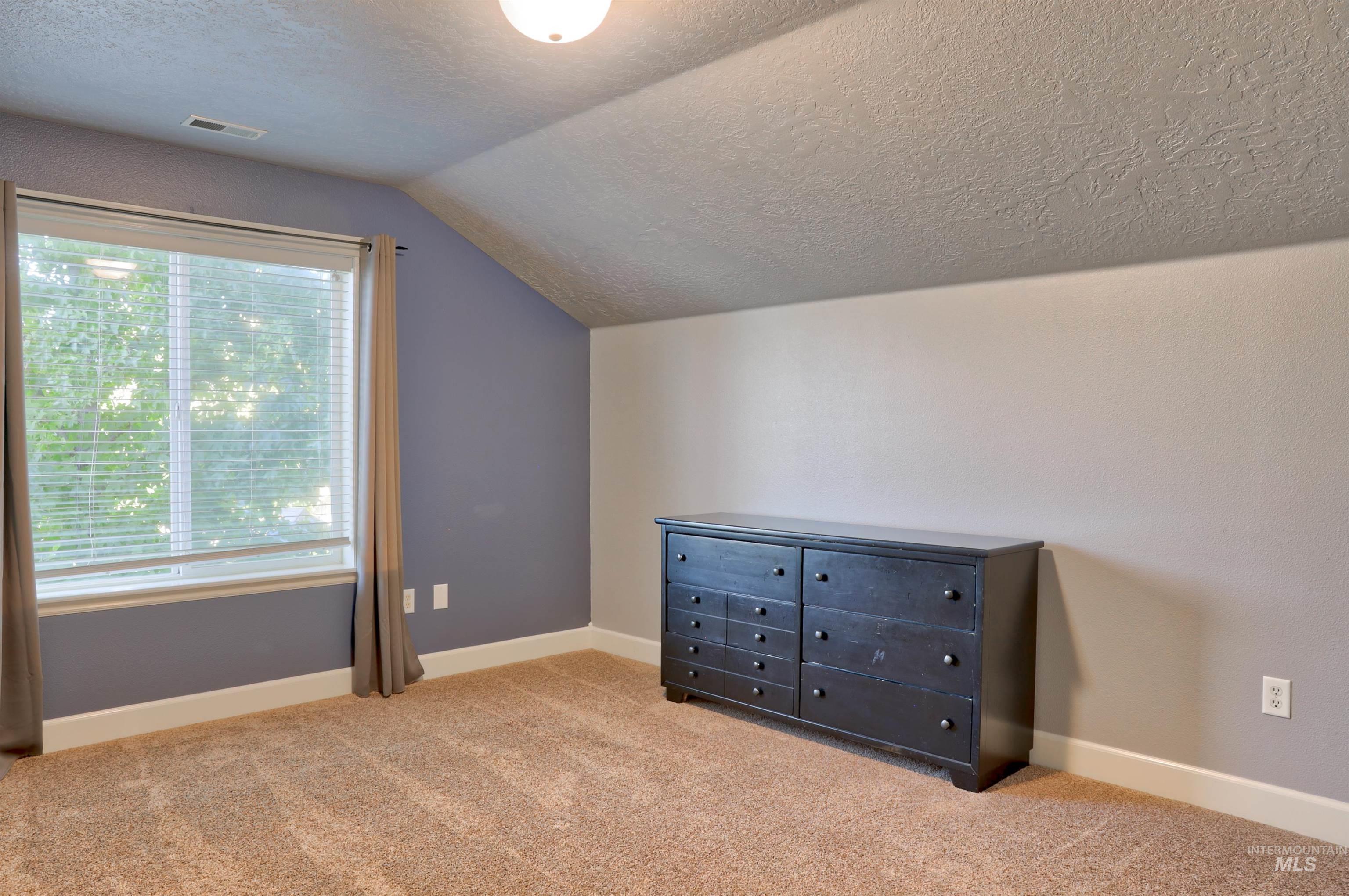 Unfurnished bedroom with a textured ceiling, light colored carpet, and vaulted ceiling