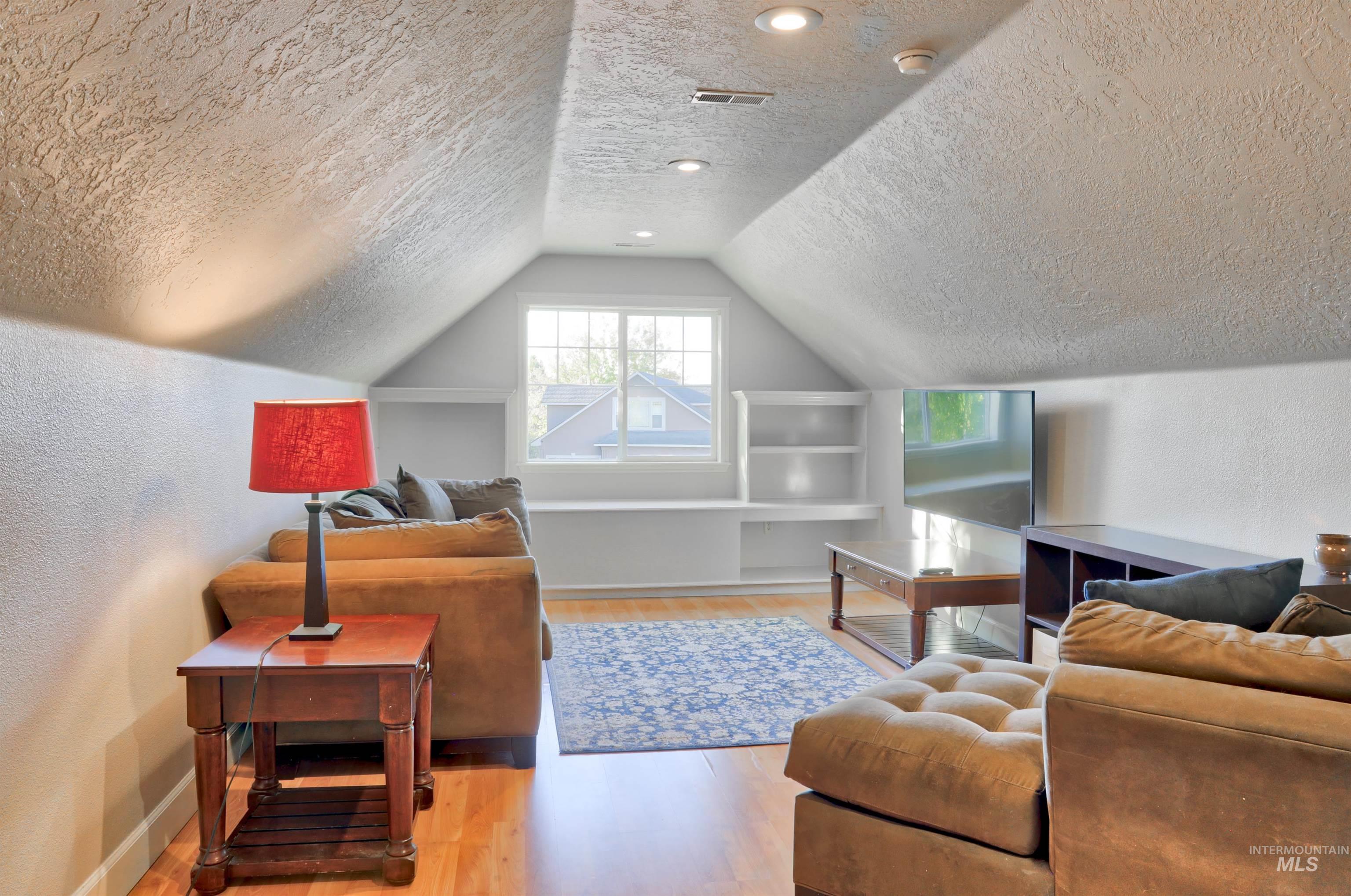 Bonus room featuring a textured wall, light wood finished floors, a textured ceiling, and vaulted ceiling