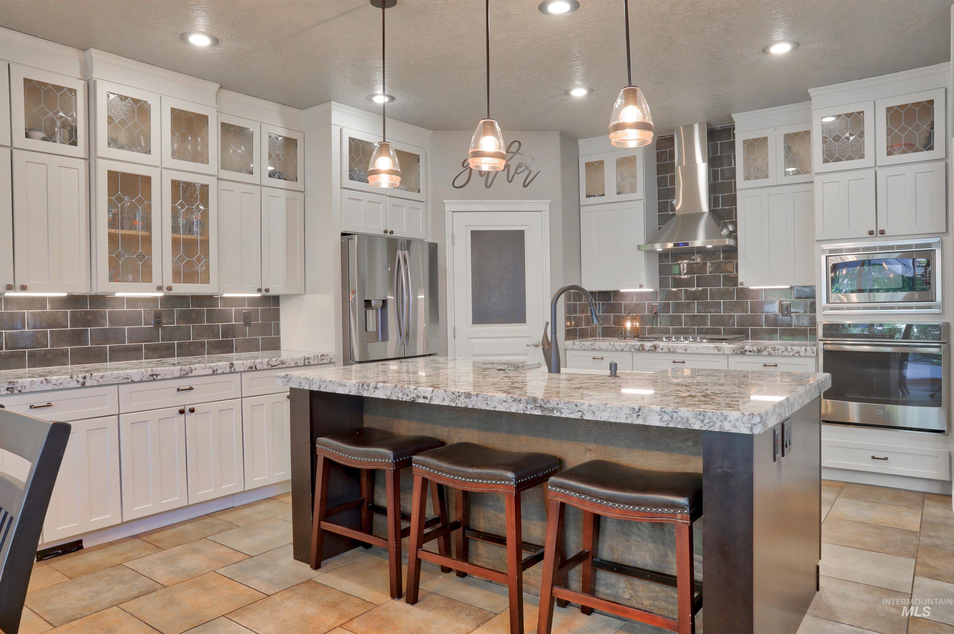 Kitchen featuring decorative backsplash, glass insert cabinets, appliances with stainless steel finishes, wall chimney exhaust hood, and recessed lighting