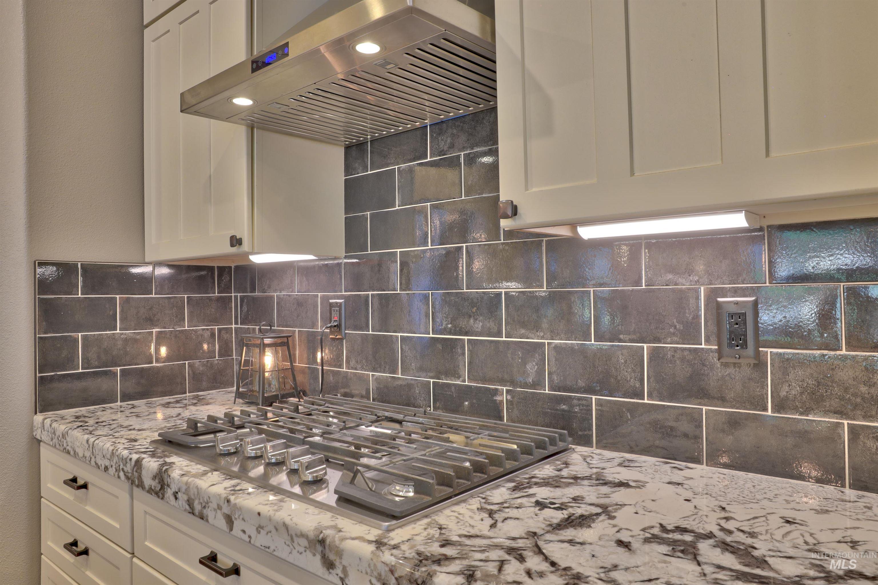 Kitchen view of extractor fan, backsplash, stainless steel gas cooktop, and white cabinets
