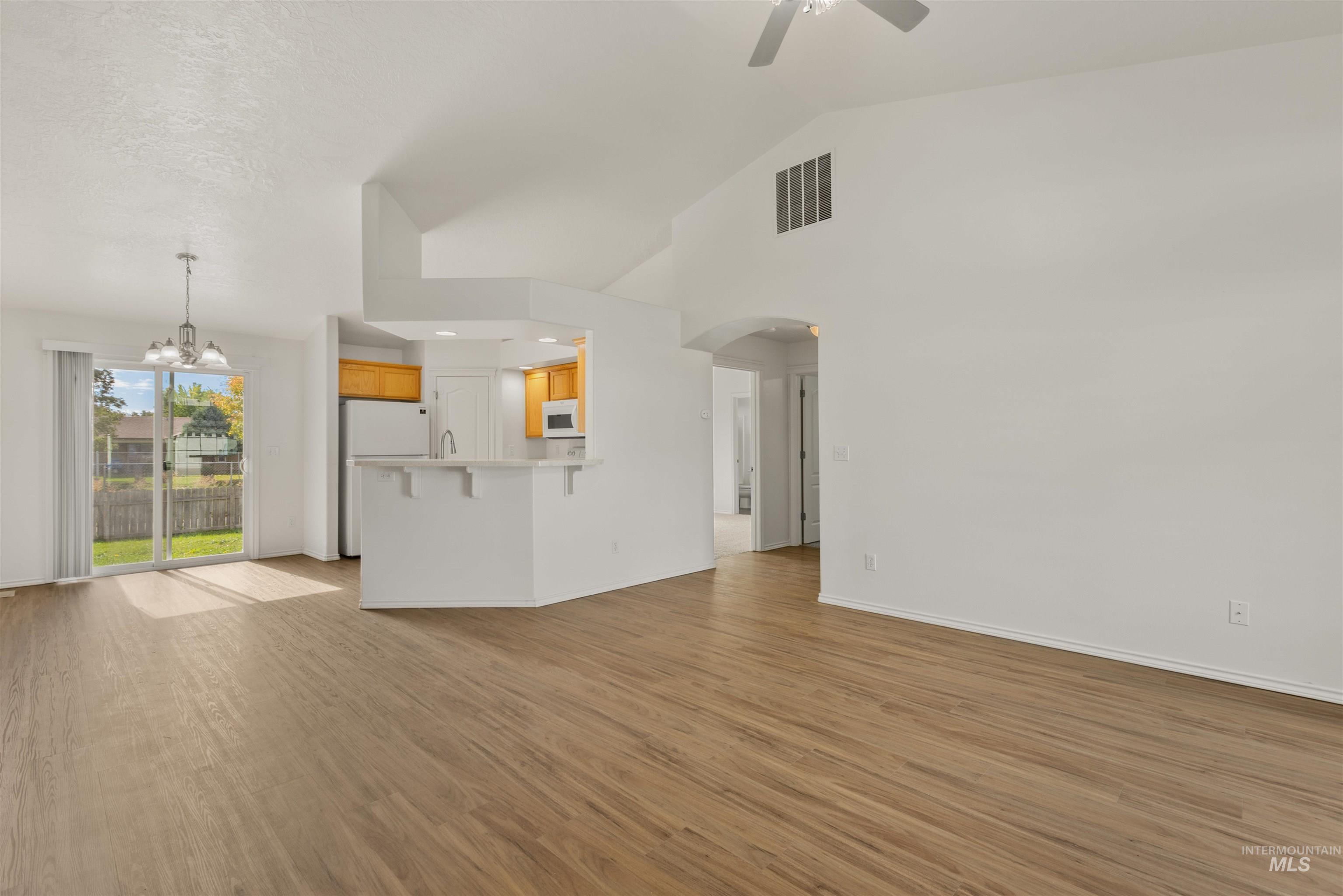 Unfurnished living room featuring light wood-style flooring, a chandelier, arched walkways, high vaulted ceiling, and a ceiling fan