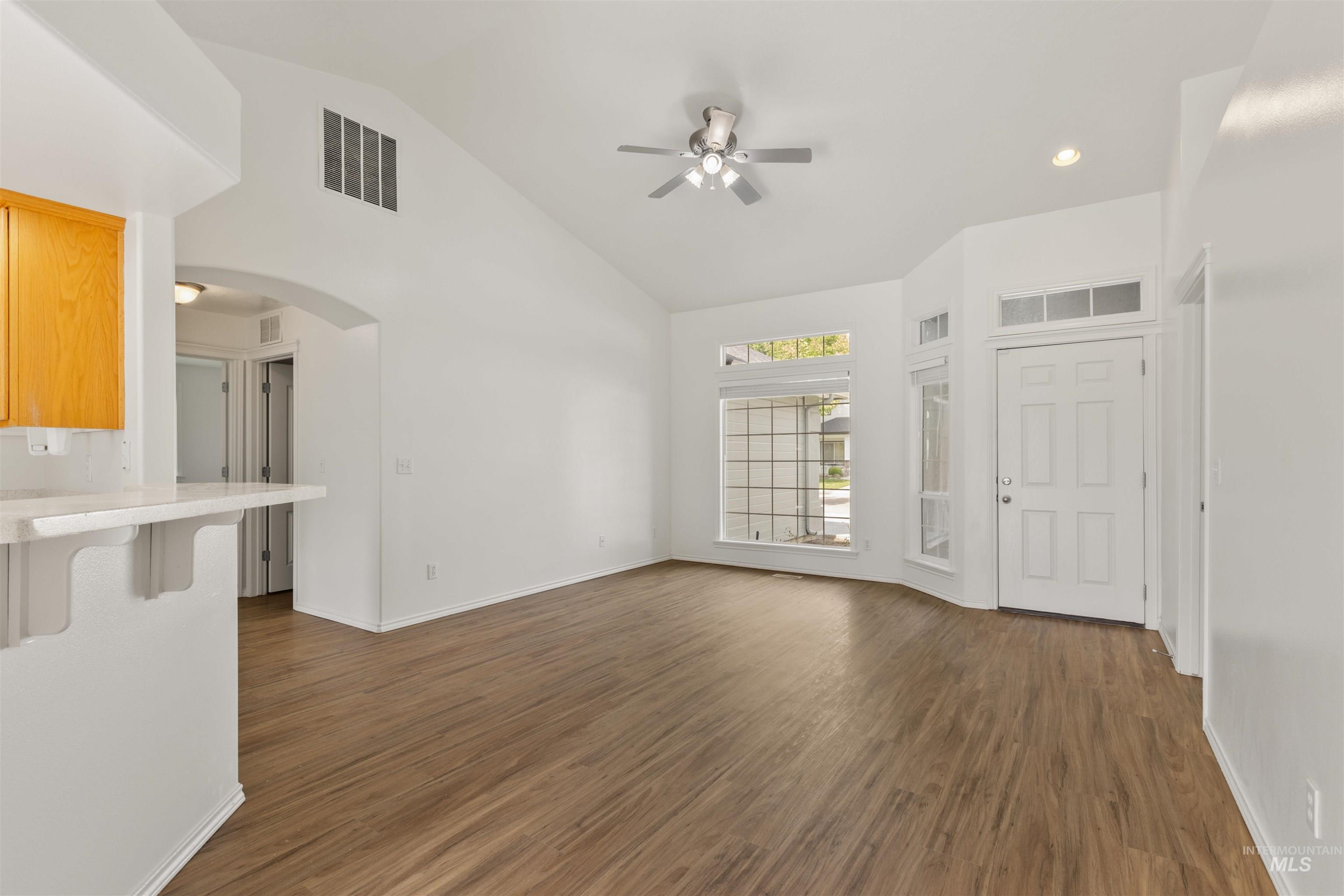 Unfurnished living room with dark wood finished floors, ceiling fan, arched walkways, high vaulted ceiling, and recessed lighting