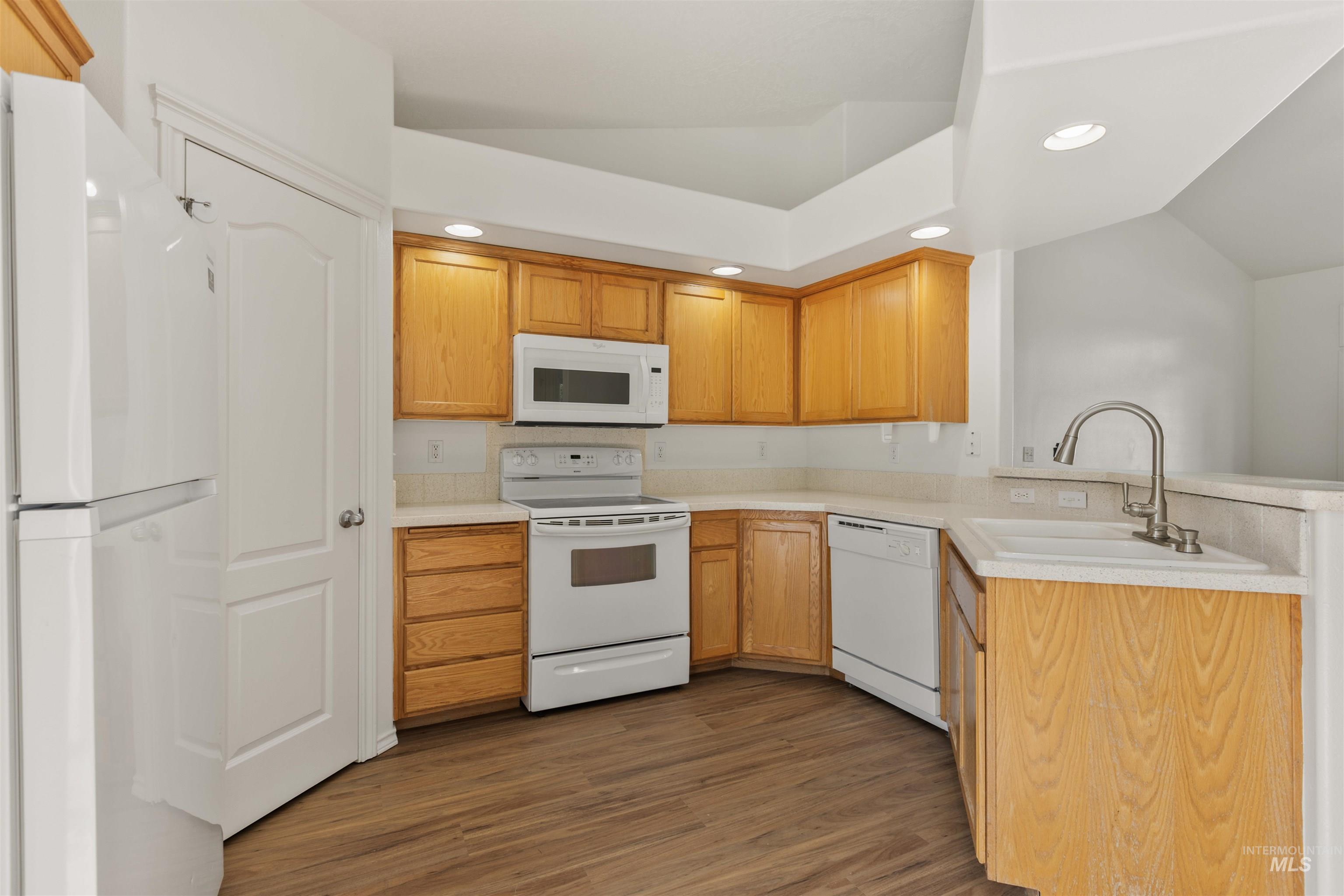 Kitchen with white appliances, lofted ceiling, dark wood finished floors, recessed lighting, and light countertops