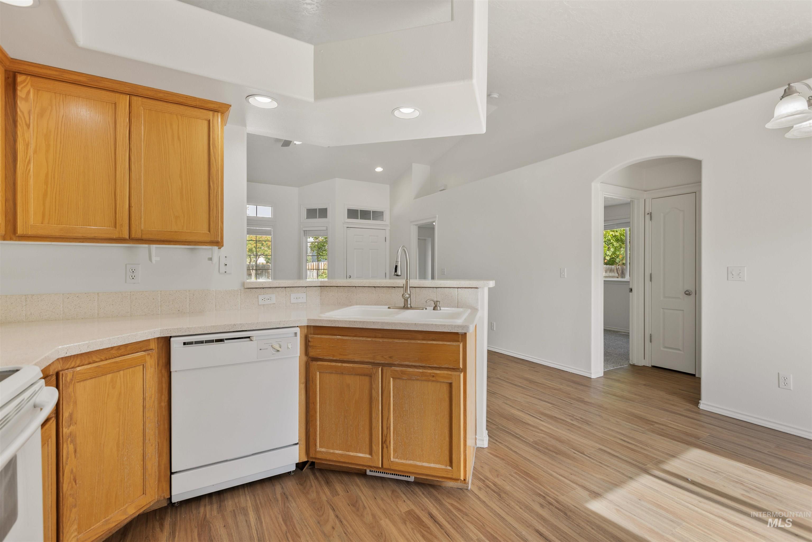 Kitchen featuring recessed lighting, arched walkways, white appliances, a peninsula, and light wood finished floors