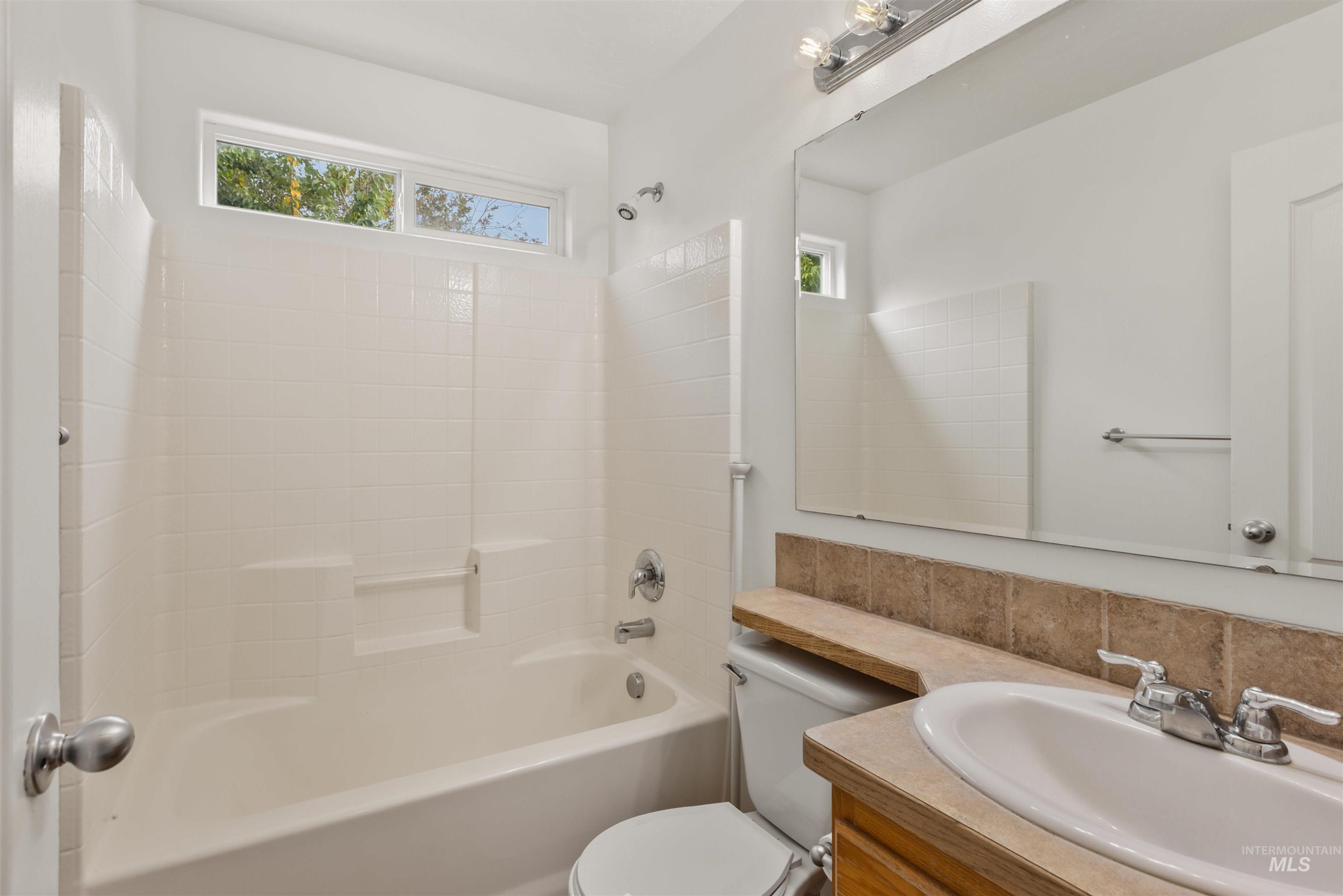 Bathroom featuring shower / washtub combination, vanity, plenty of natural light, and tasteful backsplash