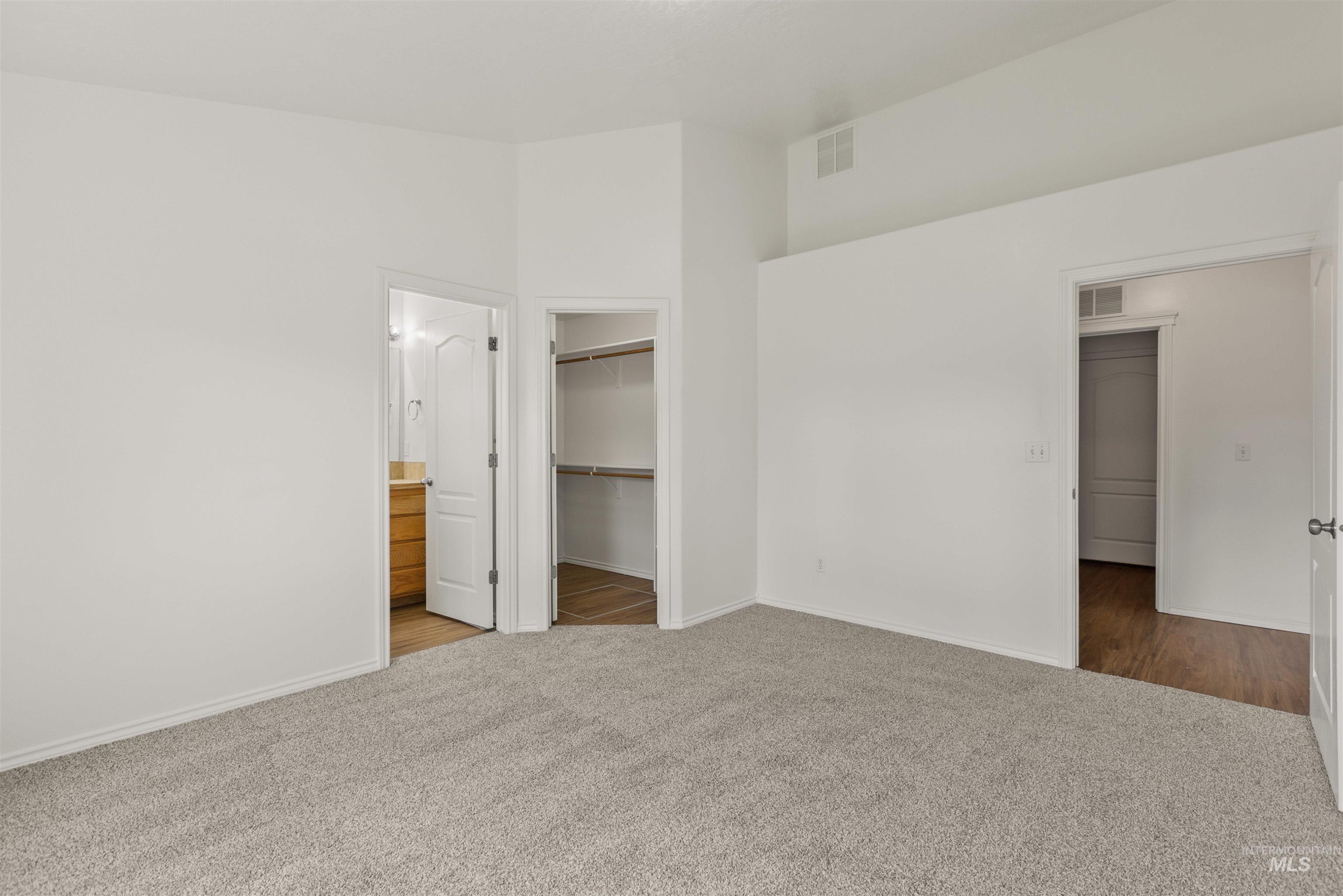 Unfurnished bedroom featuring light colored carpet, a walk in closet, and connected bathroom