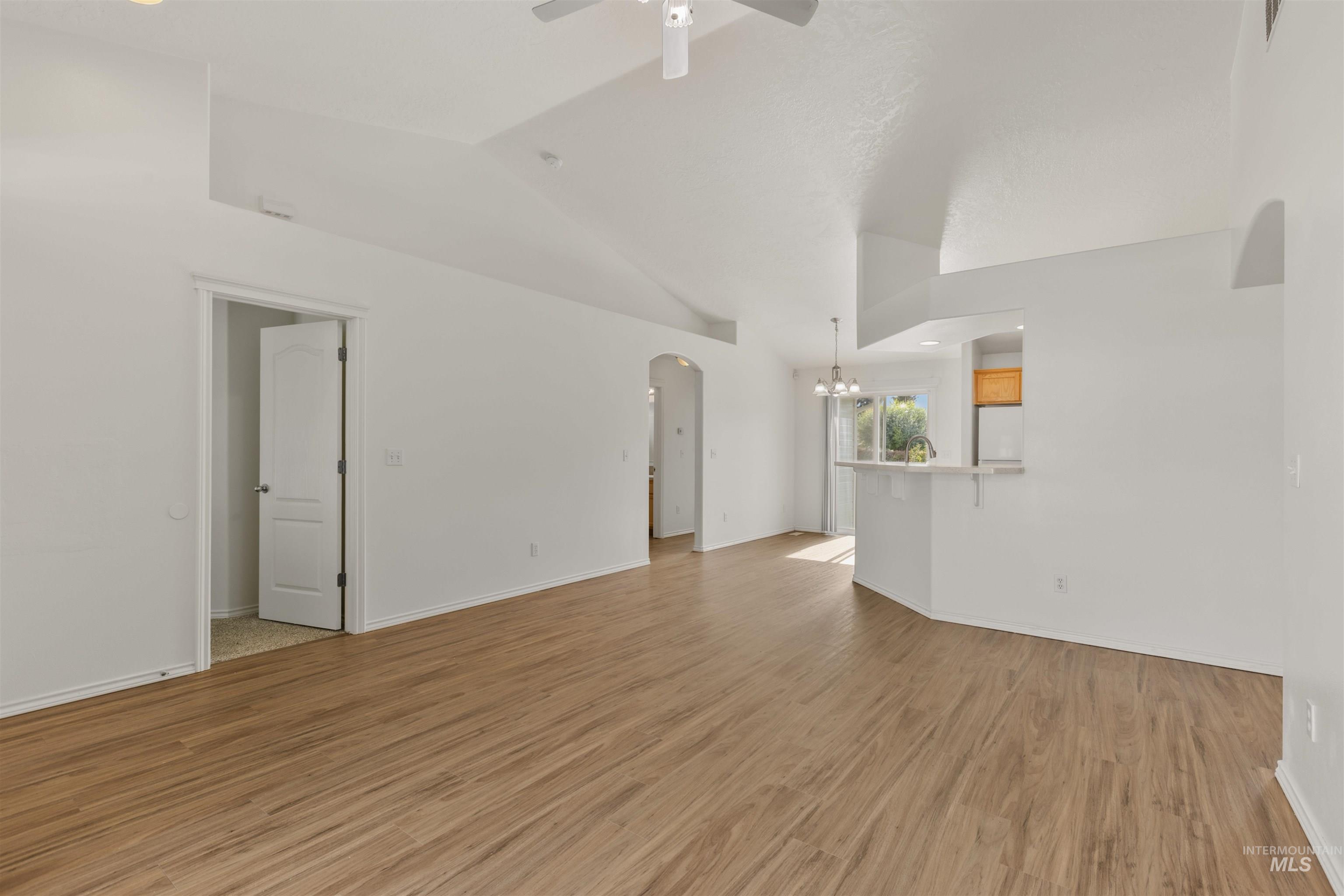 Unfurnished living room featuring arched walkways, light wood-style floors, a chandelier, vaulted ceiling, and recessed lighting