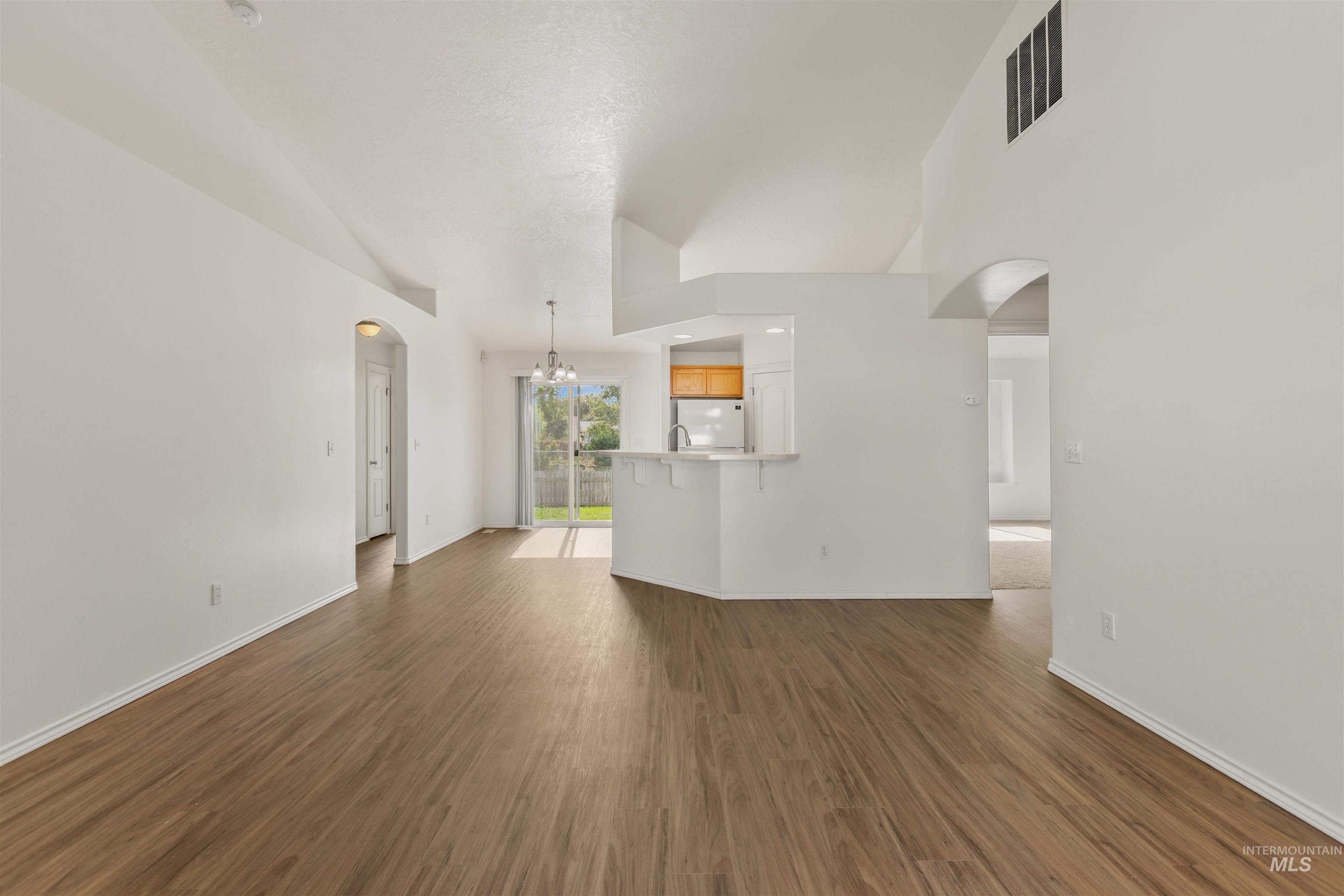 Unfurnished living room featuring arched walkways, a chandelier, dark wood-type flooring, and high vaulted ceiling
