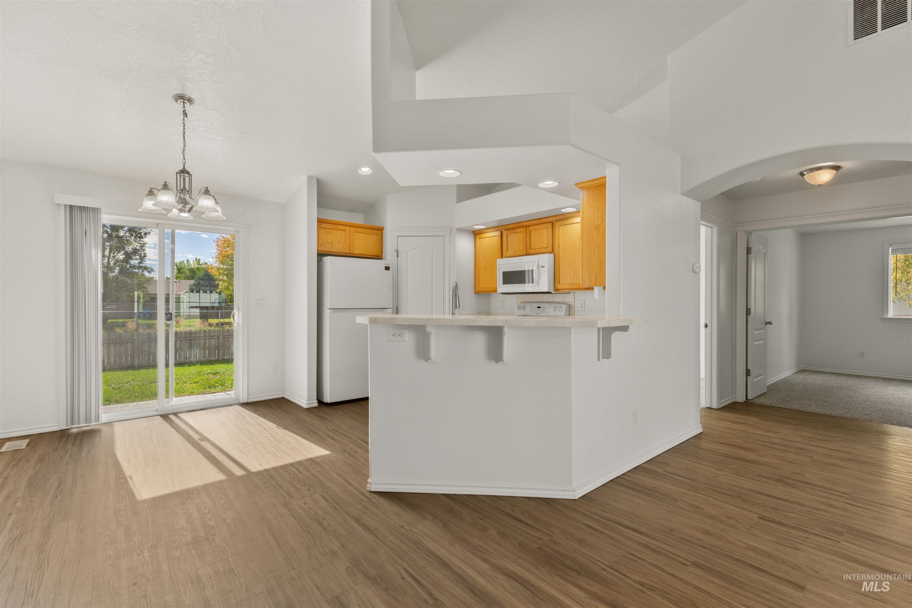 Kitchen featuring a peninsula, arched walkways, white appliances, dark wood-style flooring, and a kitchen bar