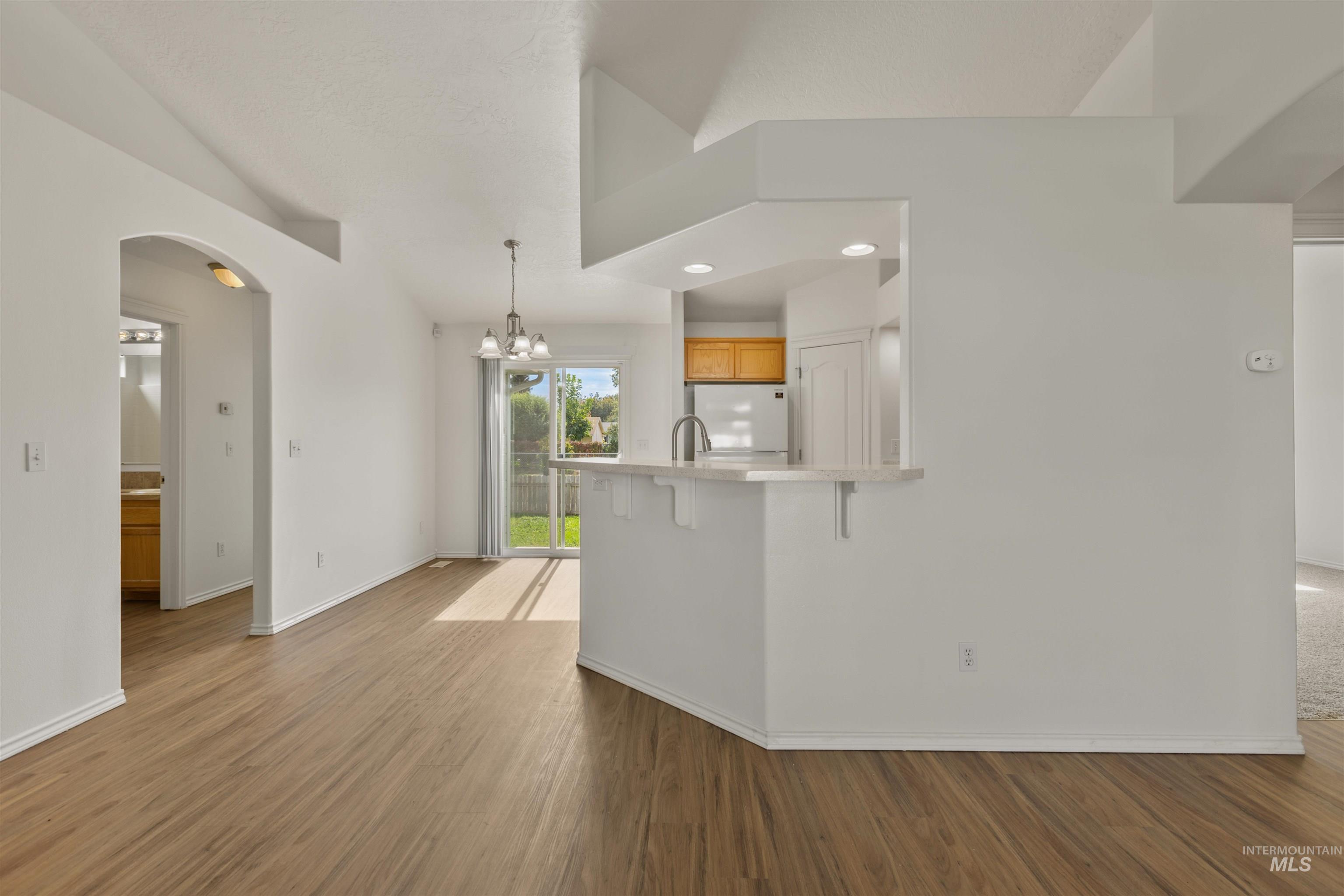 Unfurnished living room featuring dark wood finished floors, arched walkways, a chandelier, recessed lighting, and vaulted ceiling