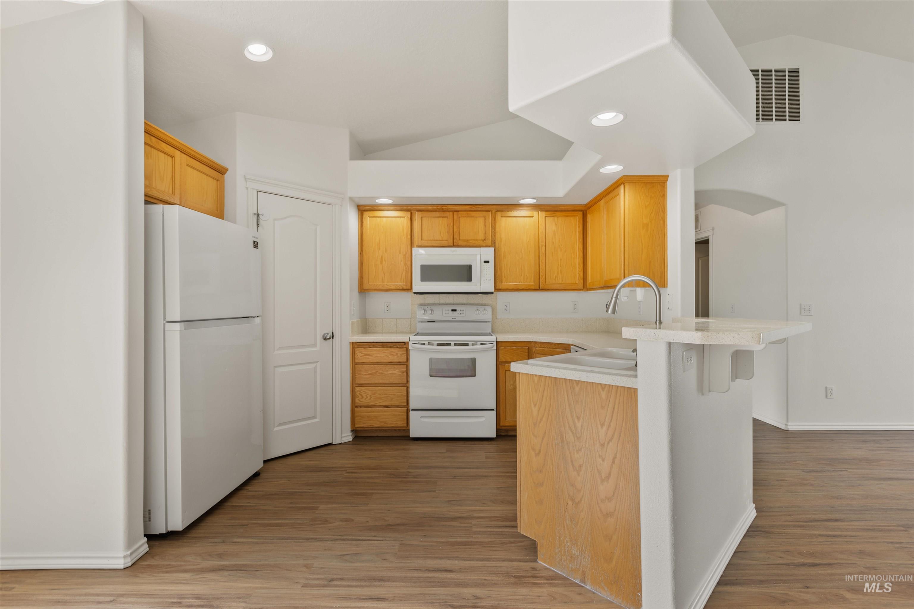 Kitchen featuring white appliances, light countertops, a breakfast bar area, light wood-style floors, and a peninsula