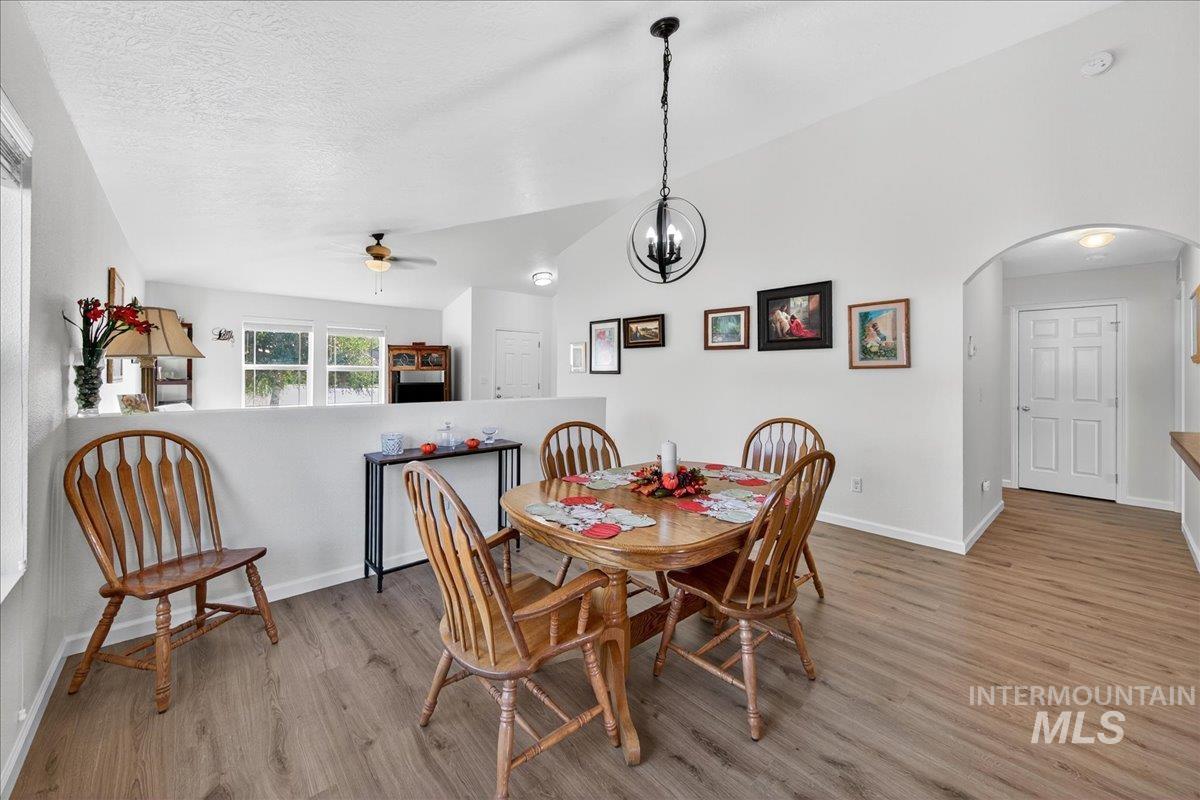 Dining space with vaulted ceiling, light wood-style floors, a chandelier, arched walkways, and a textured ceiling