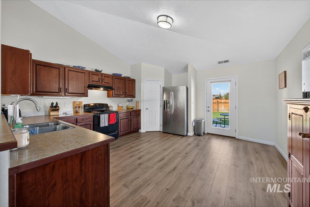Kitchen with black electric range, stainless steel refrigerator with ice dispenser, light wood-style floors, light countertops, and lofted ceiling