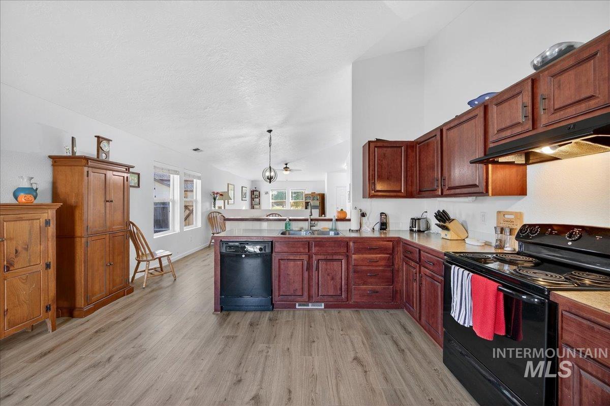 Kitchen with black appliances, a peninsula, light wood-type flooring, hanging light fixtures, and a textured ceiling