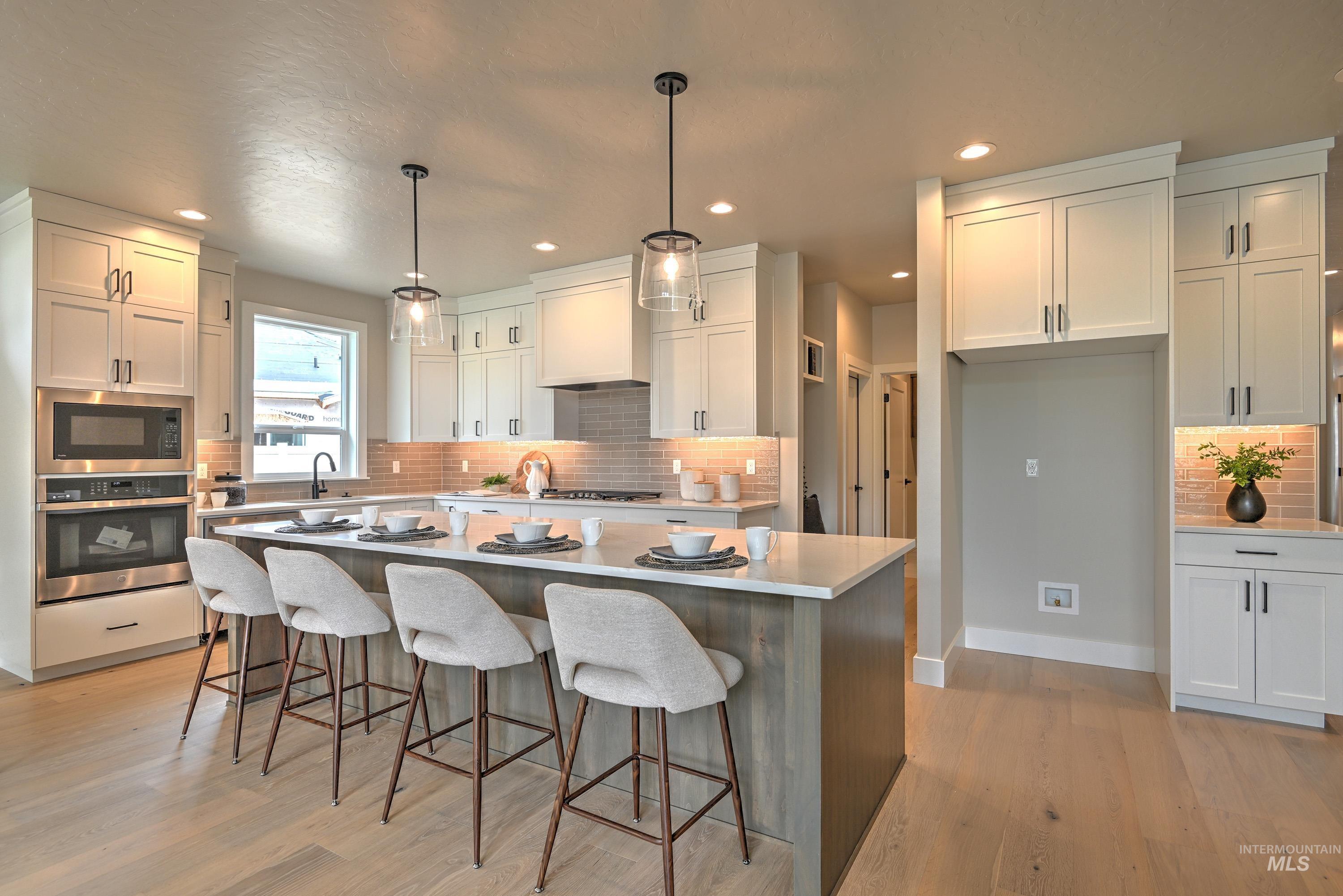 Kitchen with appliances with stainless steel finishes, tasteful backsplash, a center island, light wood-style flooring, and white cabinetry