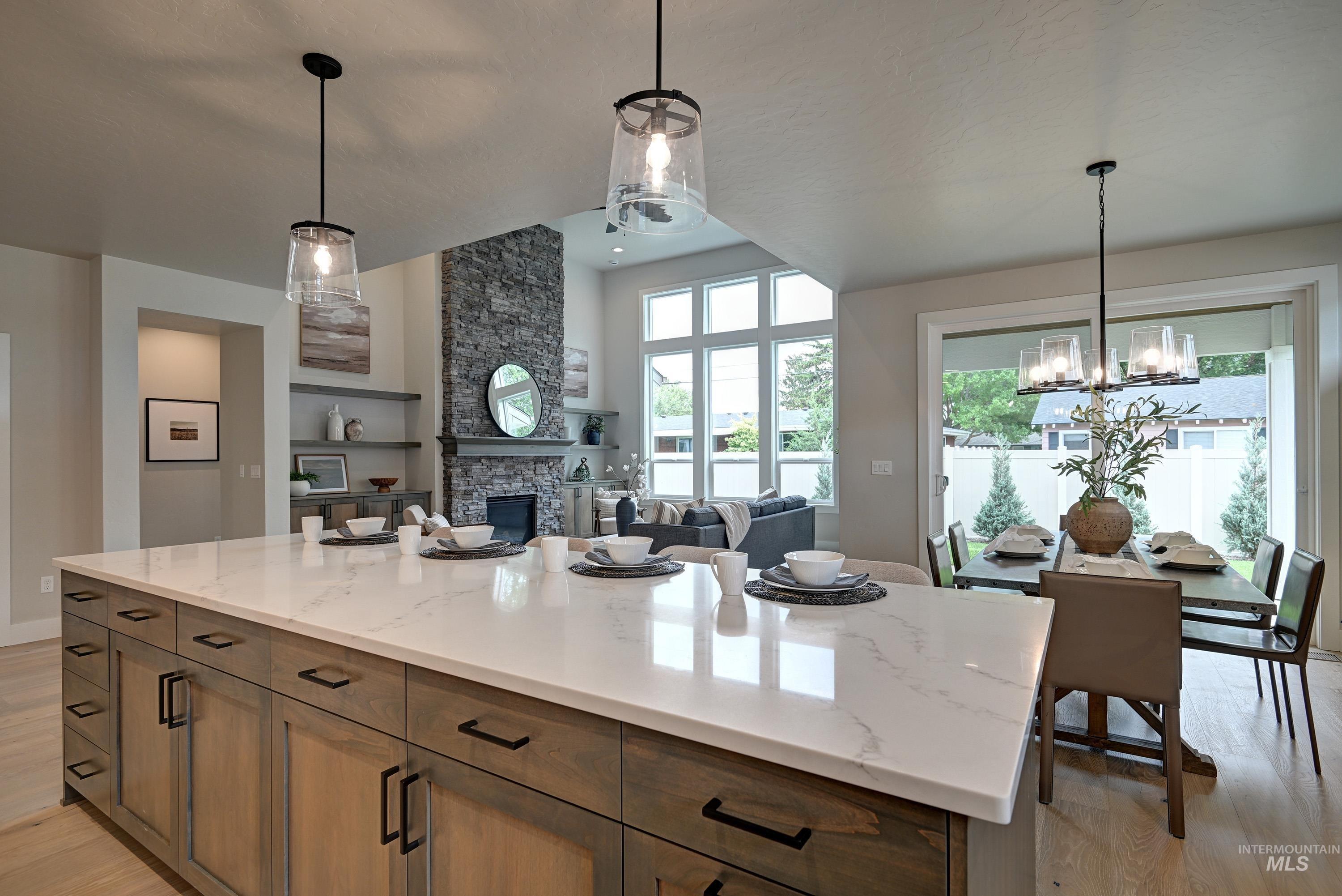 Kitchen with light wood-style floors, a chandelier, a fireplace, pendant lighting, and light stone counters