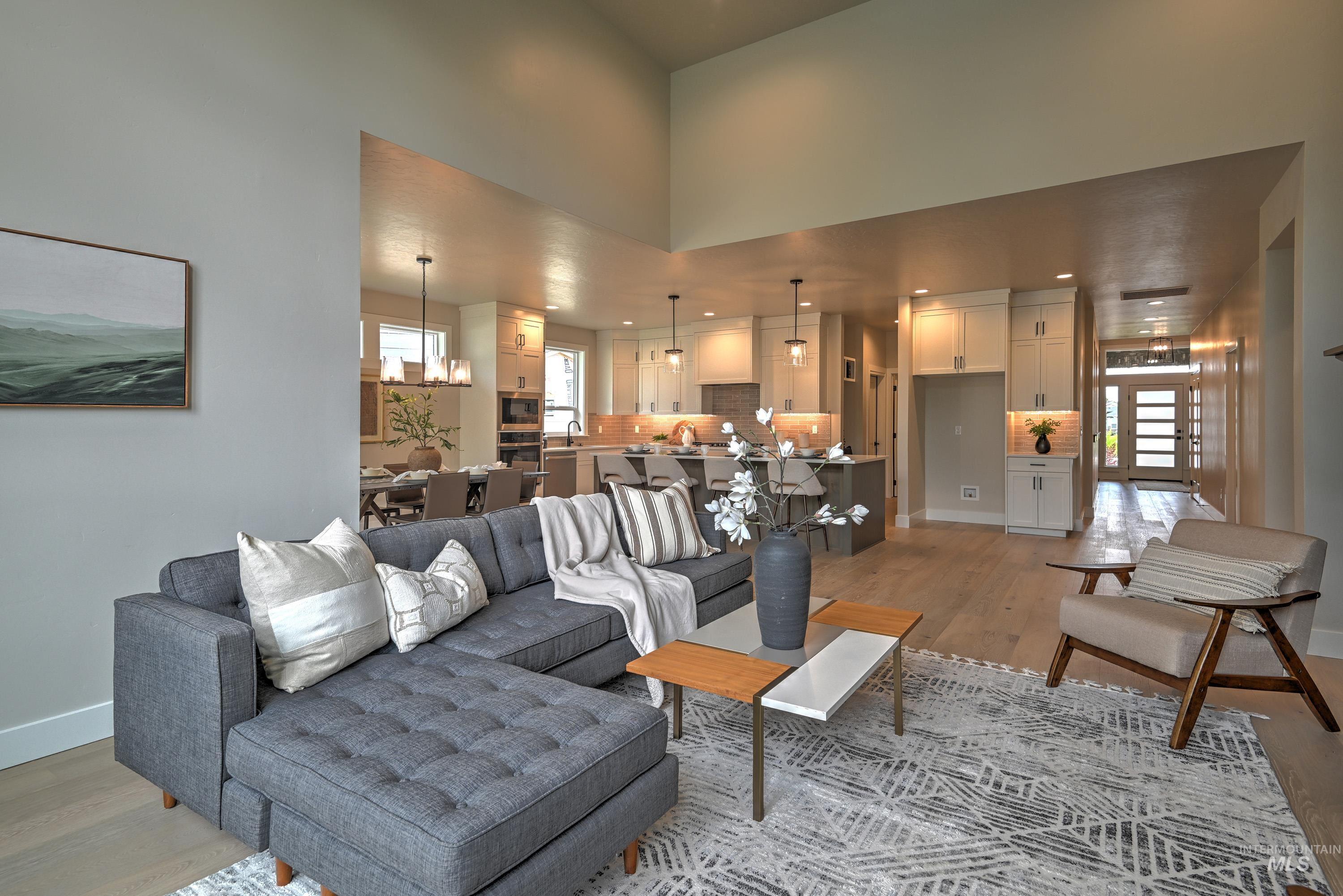Living room featuring plenty of natural light, light wood finished floors, a high ceiling, a chandelier, and recessed lighting