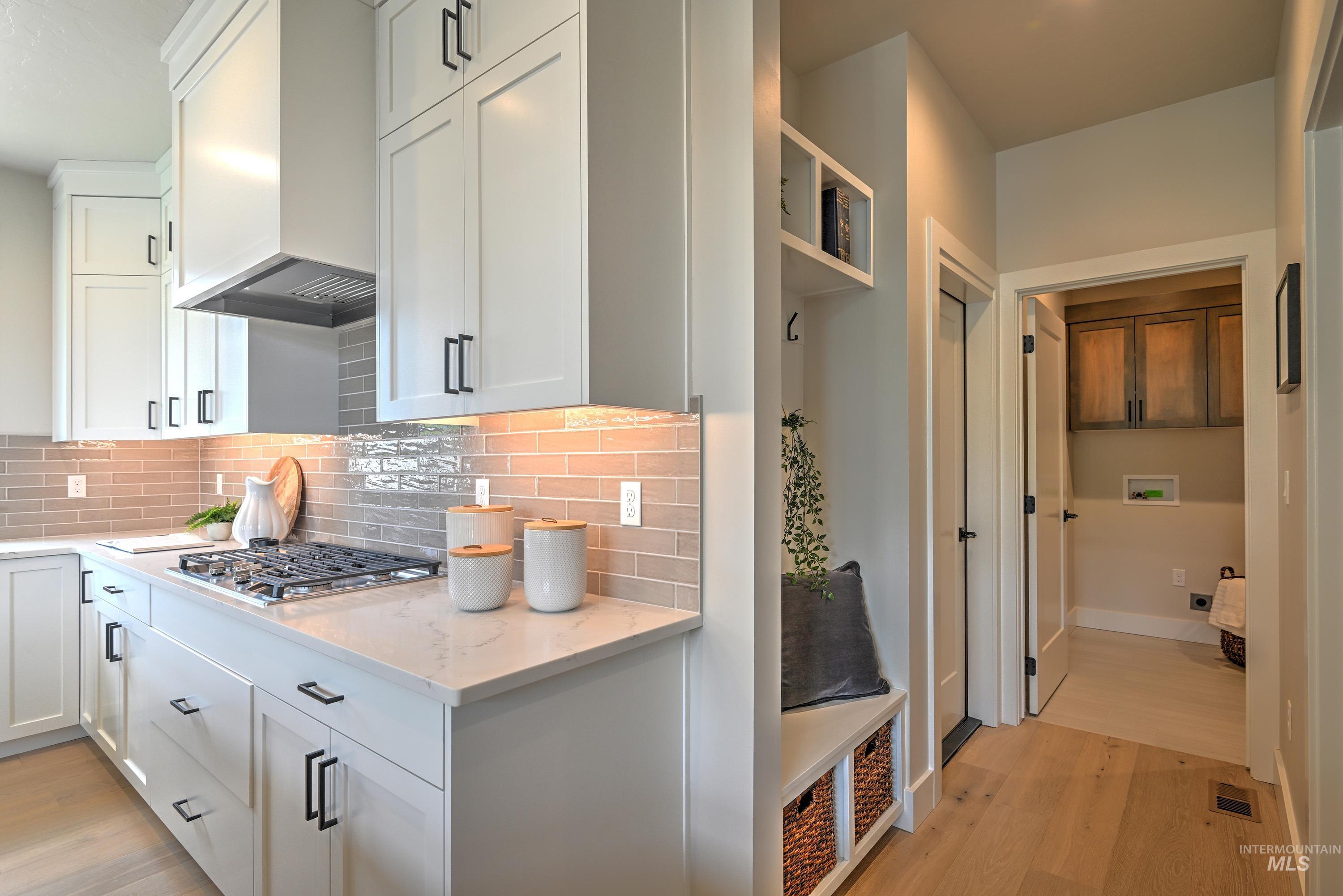 Kitchen featuring premium range hood, light wood-style floors, stainless steel gas stovetop, backsplash, and white cabinets
