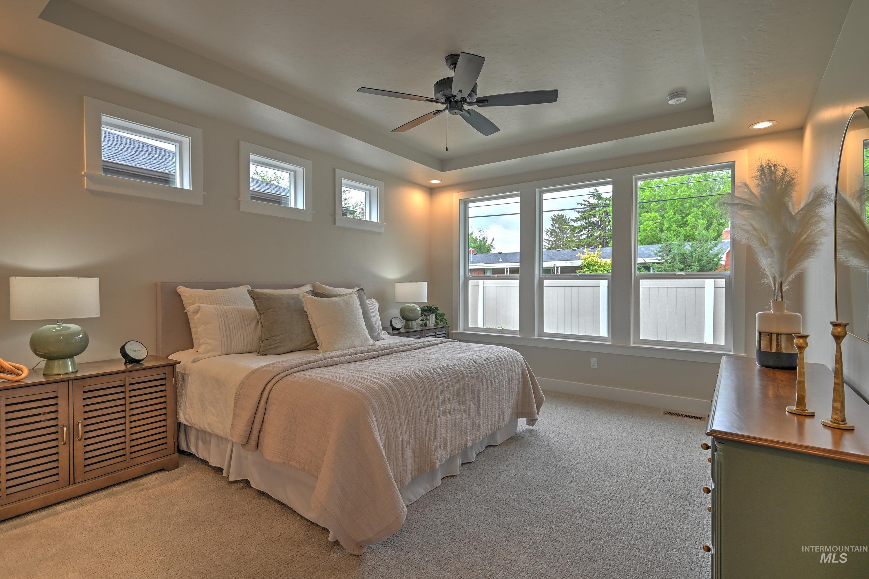 Bedroom with a raised ceiling and light colored carpet