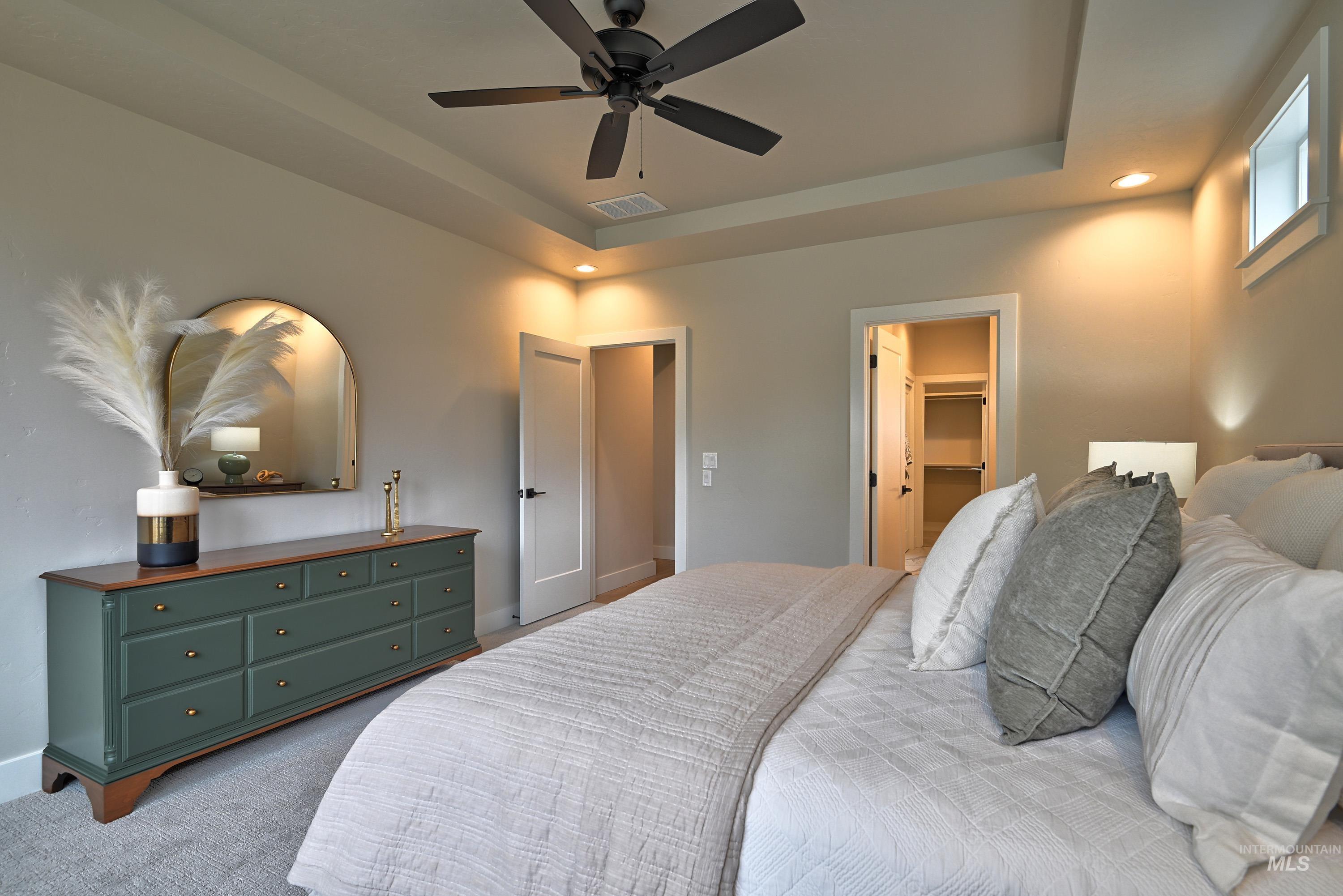 Bedroom featuring a walk in closet, a raised ceiling, light colored carpet, recessed lighting, and a ceiling fan