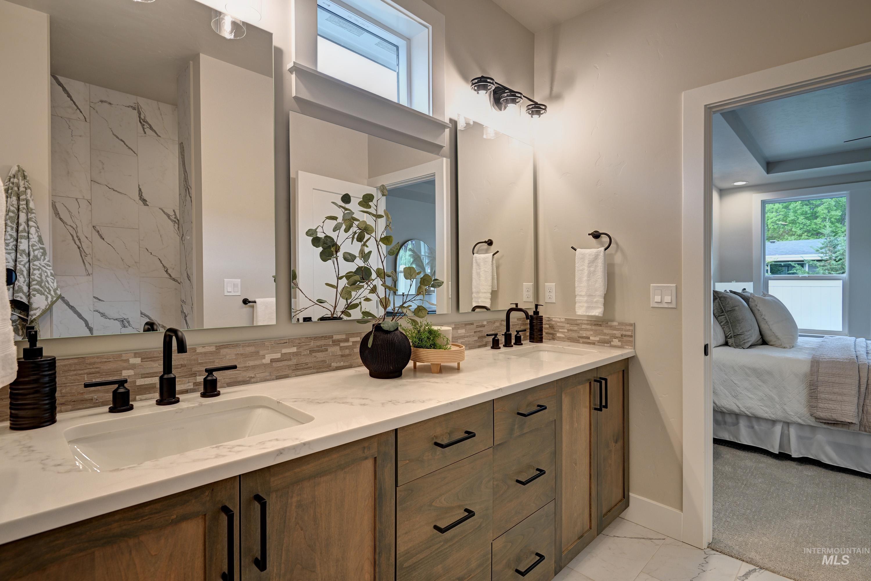 Bathroom with double vanity, ensuite bath, marble look tile flooring, and tasteful backsplash