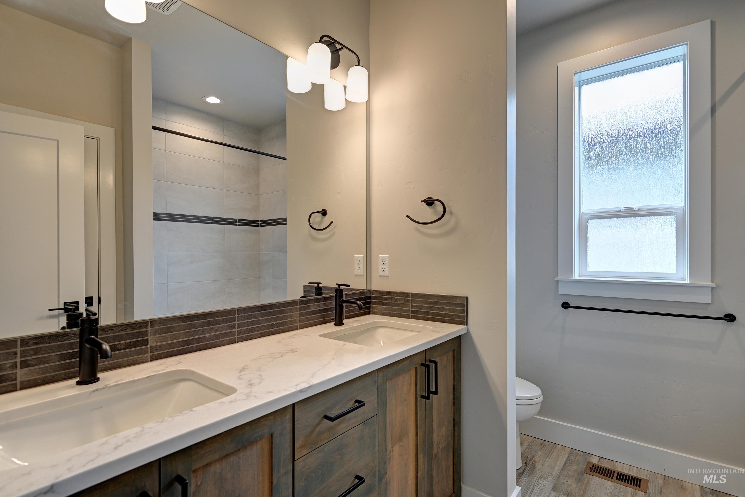 Bathroom featuring backsplash, healthy amount of natural light, double vanity, and wood finished floors