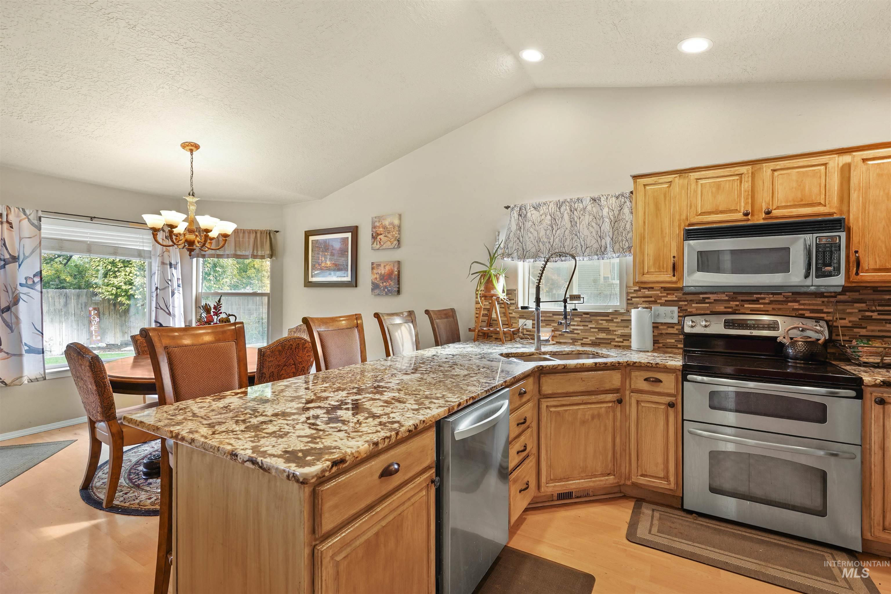 Kitchen with a peninsula, stainless steel appliances, light stone countertops, a chandelier, and vaulted ceiling