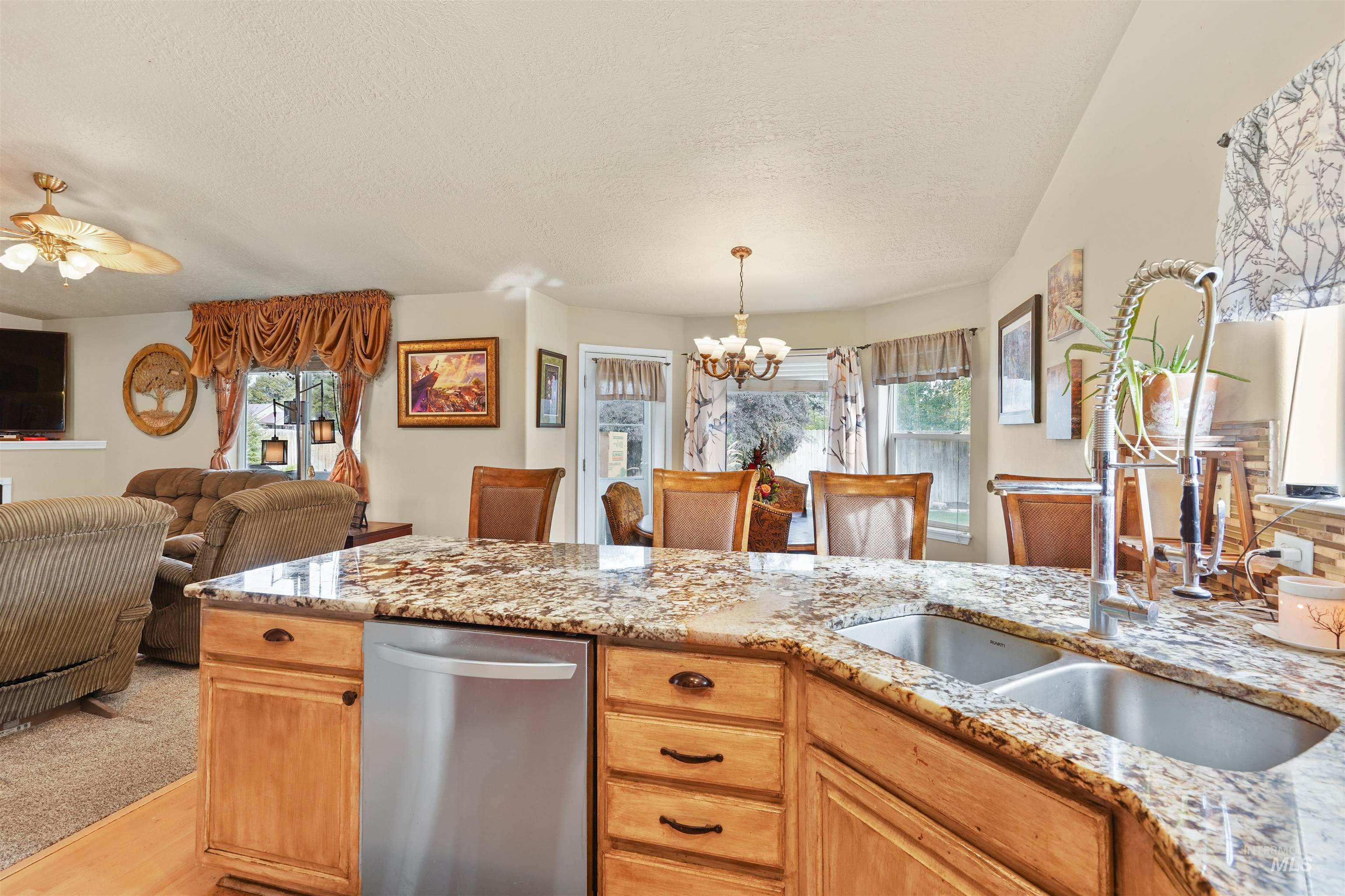 Kitchen with dishwasher, light stone counters, a chandelier, light brown cabinets, and a textured ceiling
