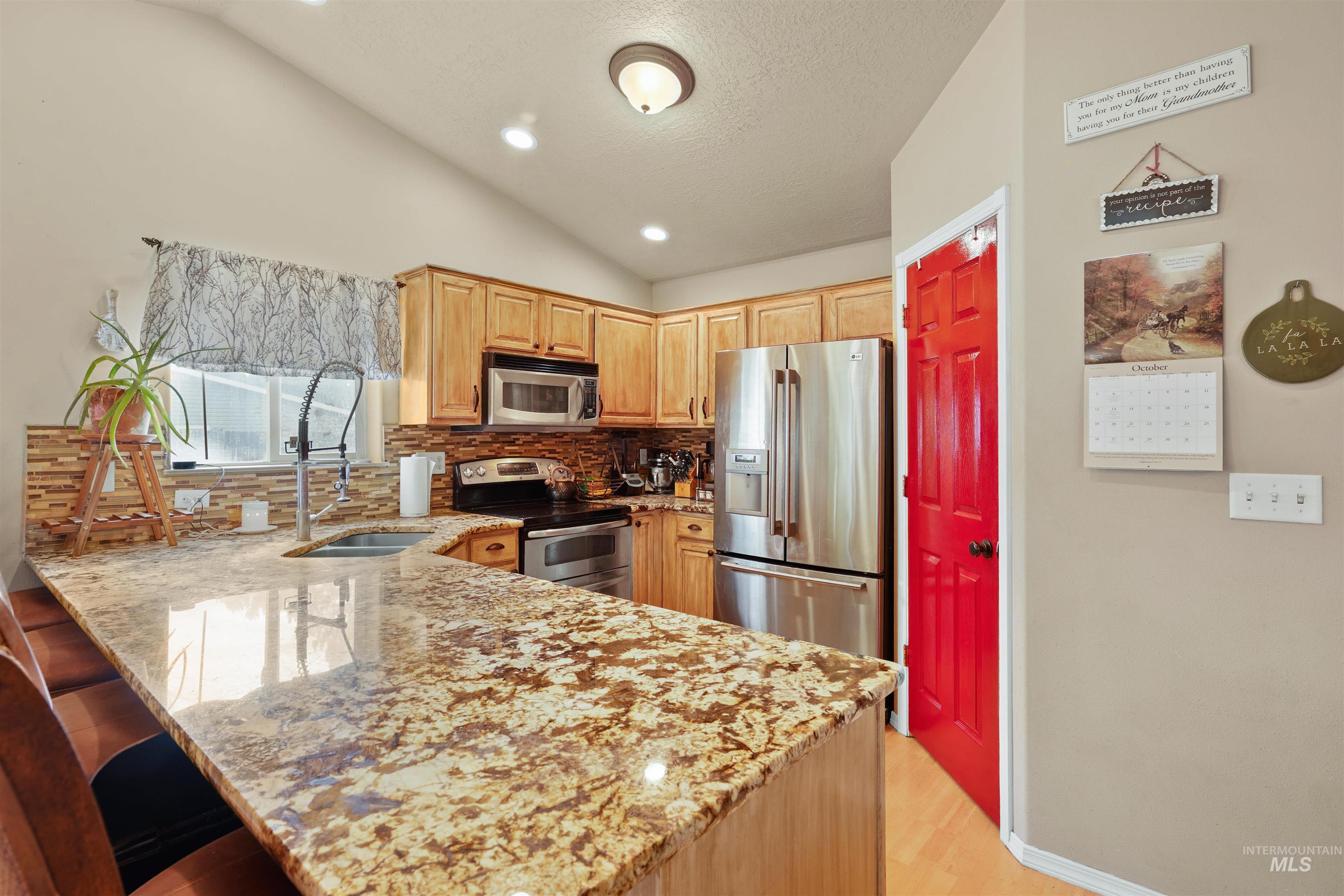 Kitchen featuring a peninsula, light brown cabinets, stainless steel appliances, backsplash, and light stone countertops