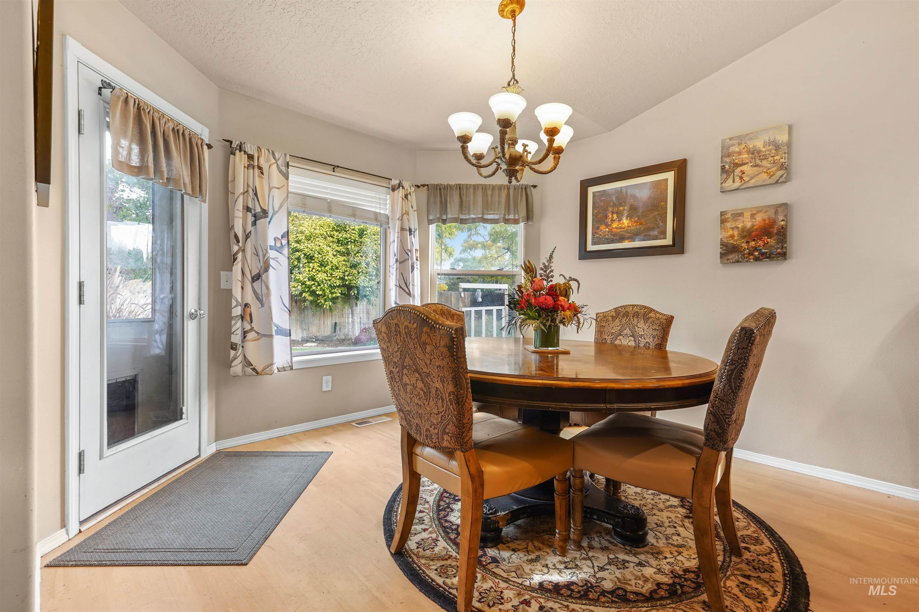 Dining space with plenty of natural light, light wood-style floors, a chandelier, vaulted ceiling, and a textured ceiling