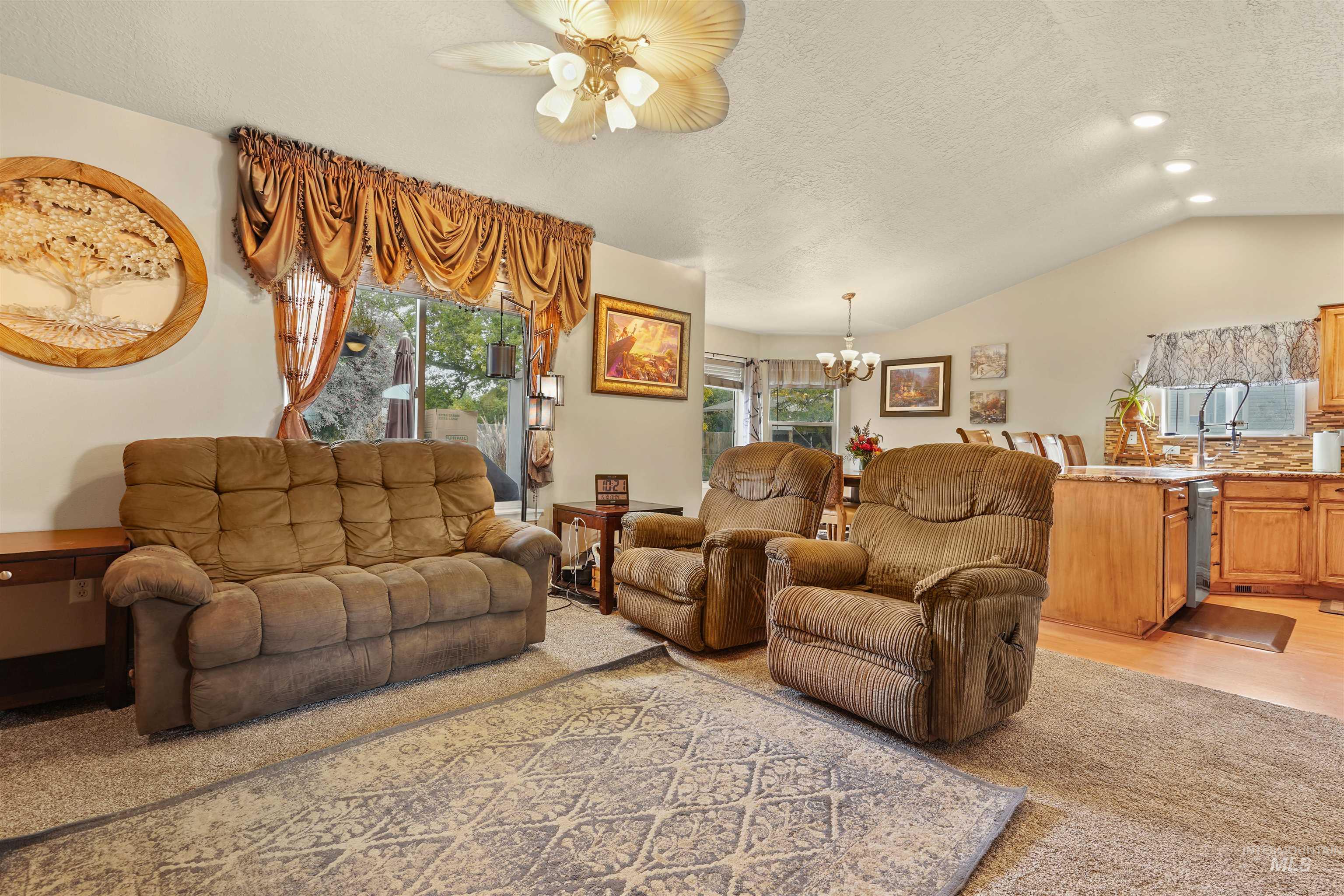 Living area with vaulted ceiling, a textured ceiling, a chandelier, light wood-style flooring, and a ceiling fan