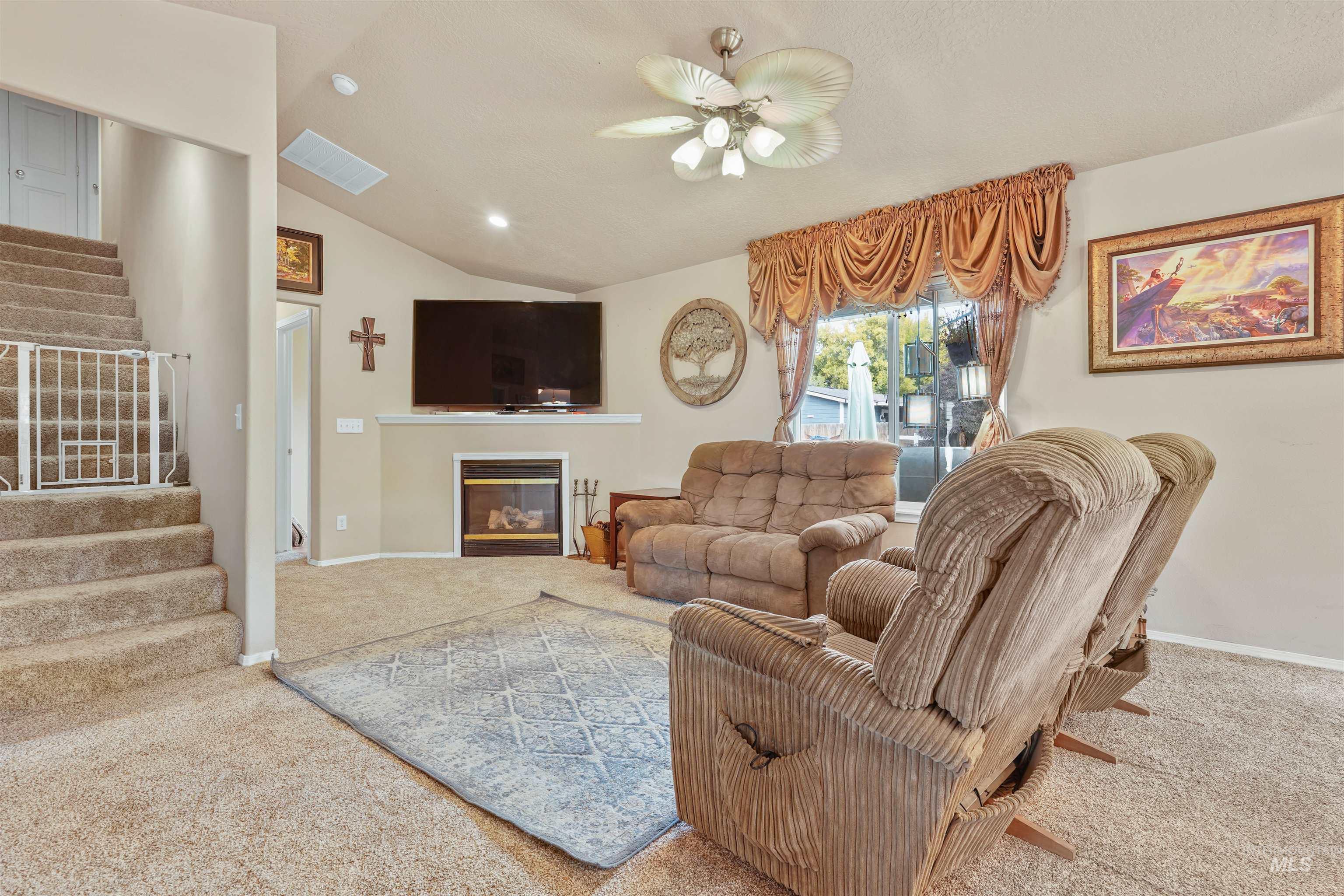Carpeted living area with a glass covered fireplace, lofted ceiling, stairway, recessed lighting, and a ceiling fan