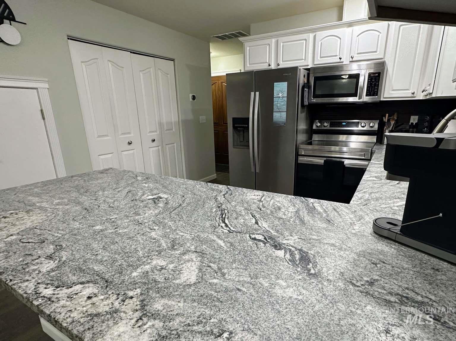 Kitchen featuring light stone counters, stainless steel appliances, and white cabinetry