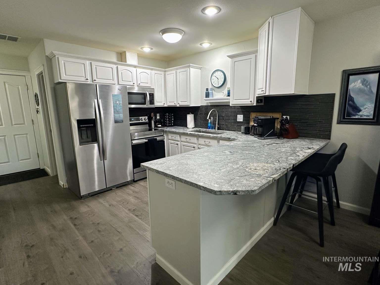 Kitchen featuring appliances with stainless steel finishes, tasteful backsplash, a peninsula, and dark wood finished floors