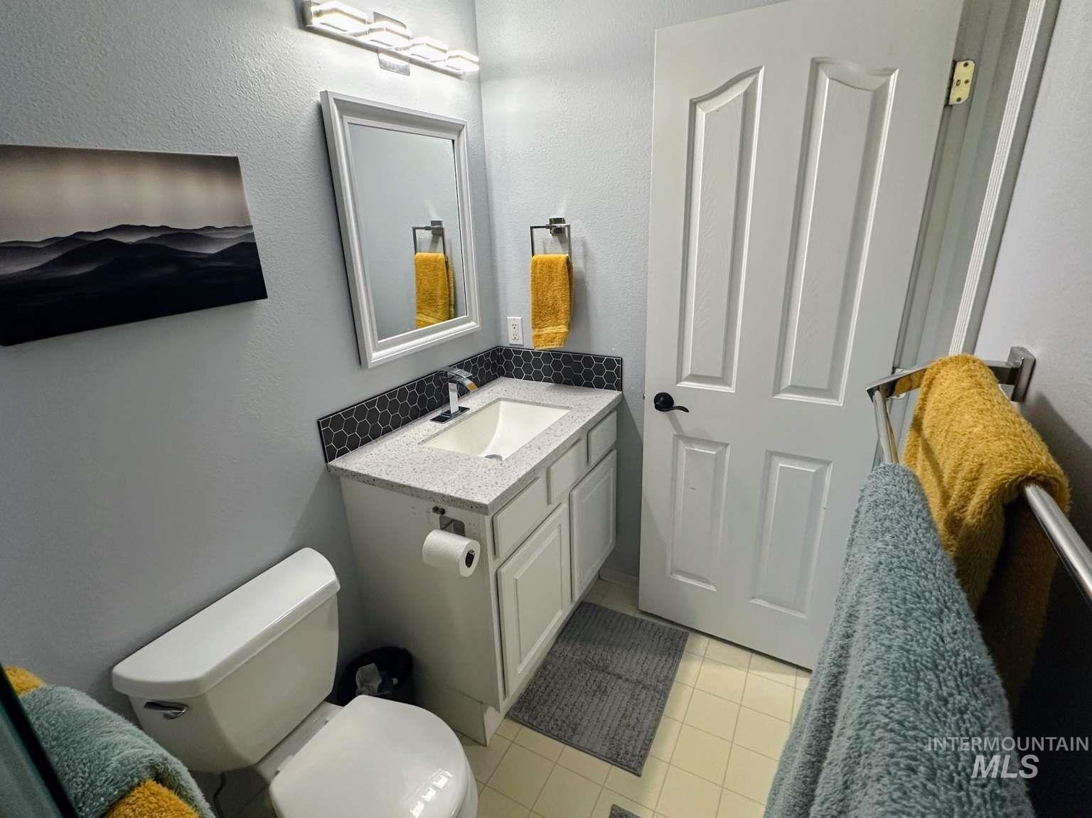 Bathroom with light tile patterned floors, vanity, a textured wall, and decorative backsplash