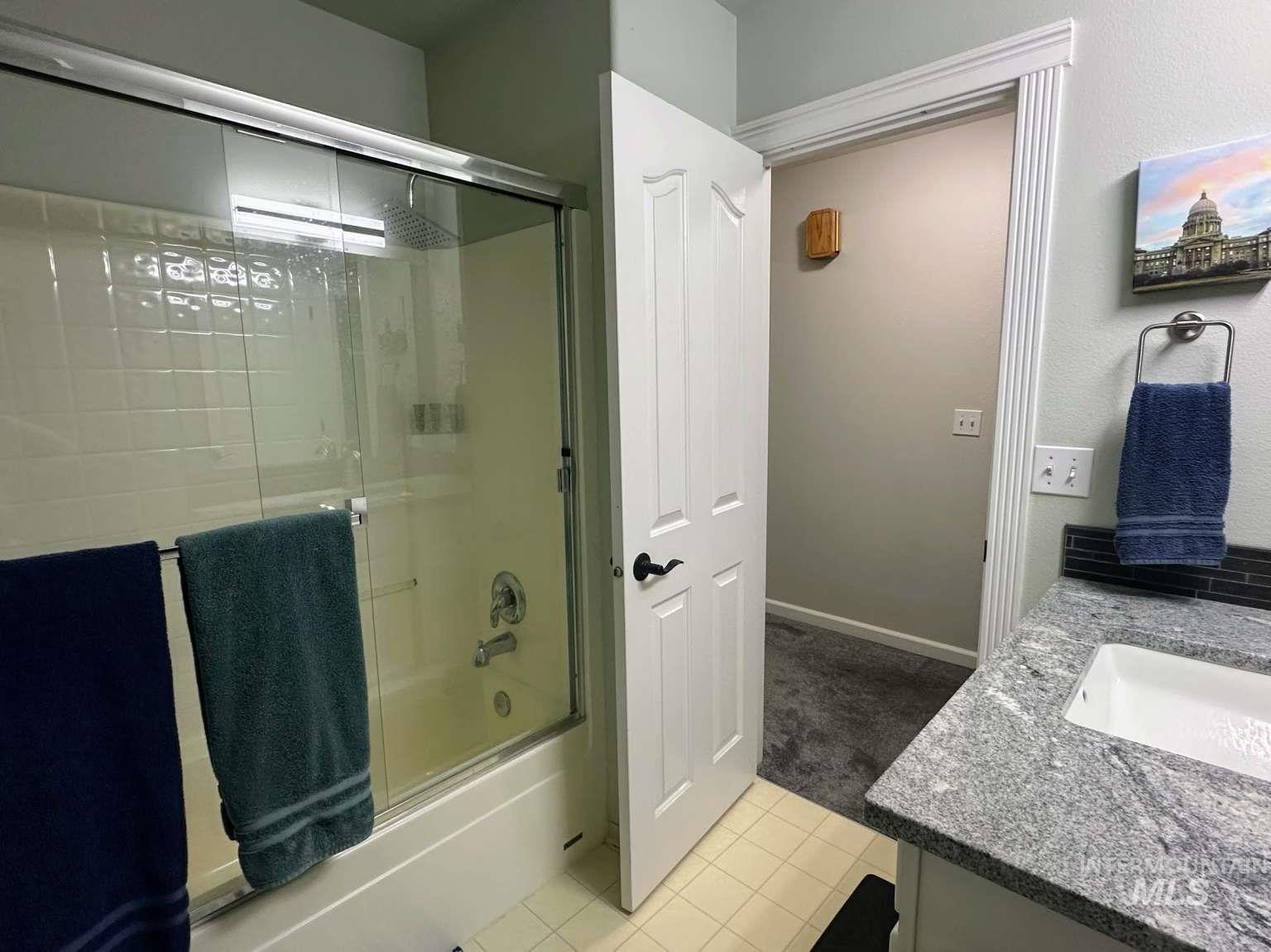 Full bath with bath / shower combo with glass door, light tile patterned floors, vanity, and light colored carpet