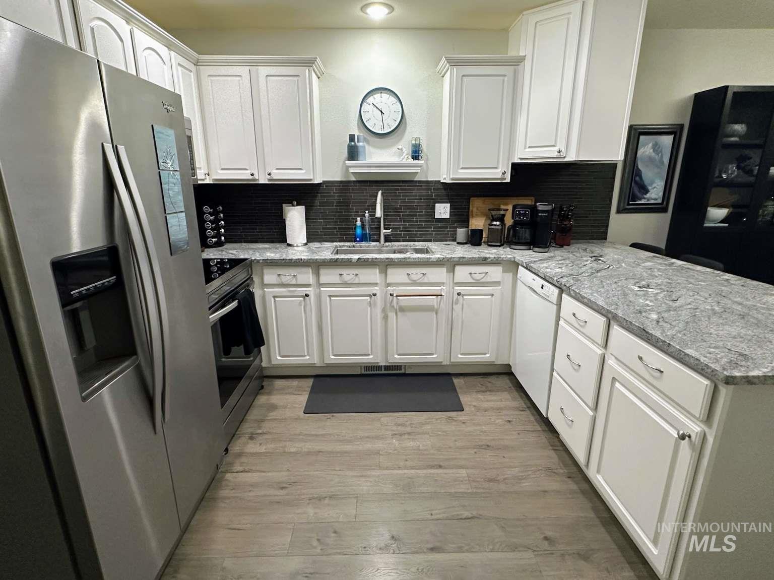 Kitchen featuring stainless steel appliances, white cabinetry, a peninsula, and decorative backsplash