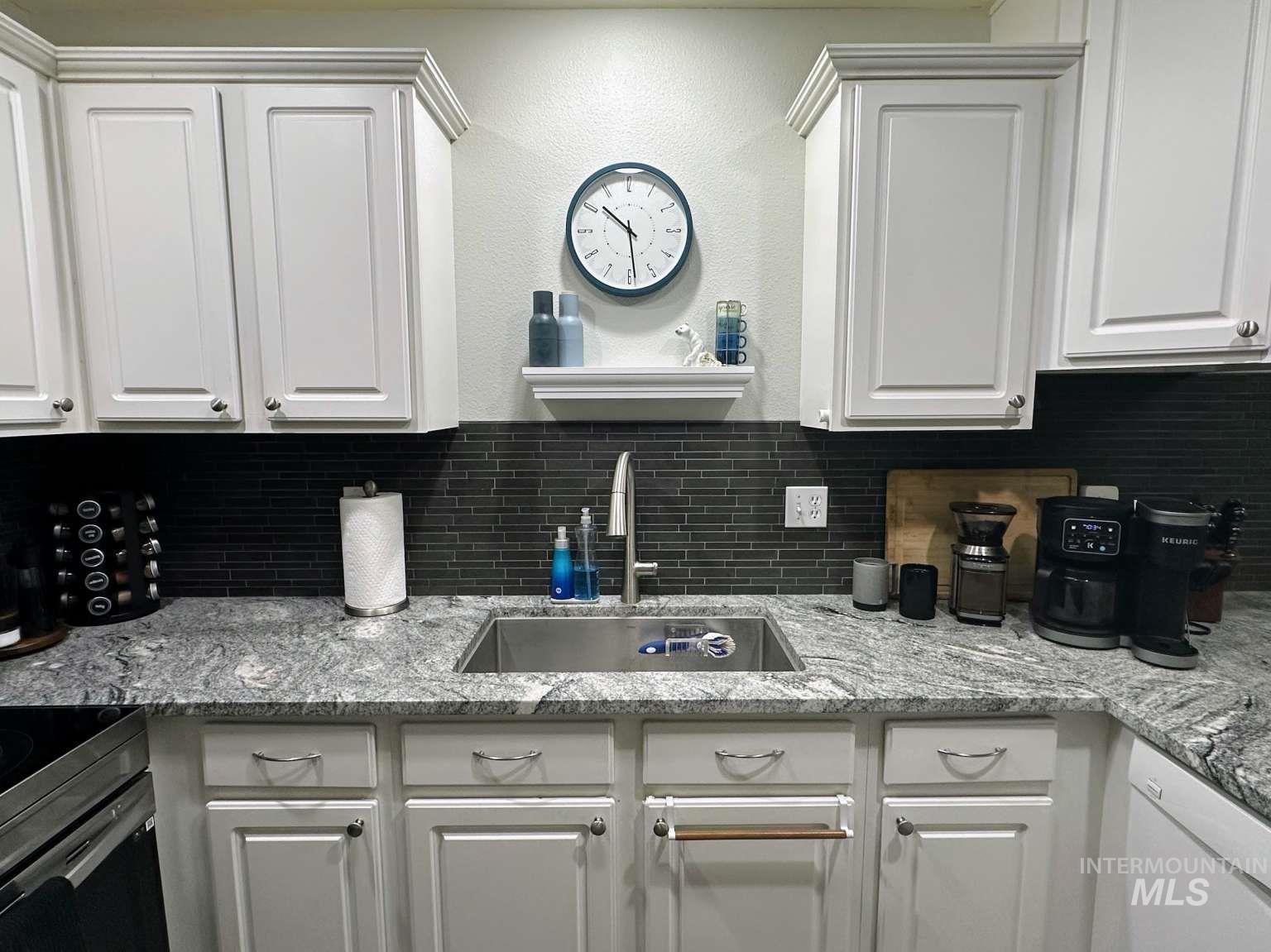 Kitchen with tasteful backsplash, light stone countertops, white cabinetry, stainless steel range with electric stovetop, and a textured wall