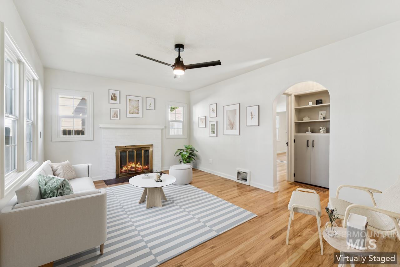 Living room featuring wood finished floors, a fireplace, ceiling fan, and arched walkways