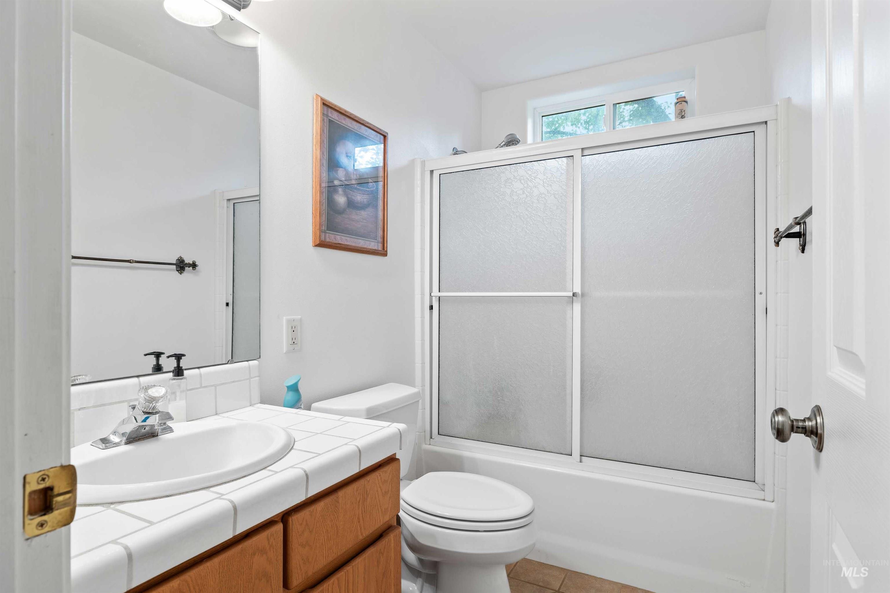 Bathroom with bath / shower combo with glass door, vanity, and light tile patterned flooring