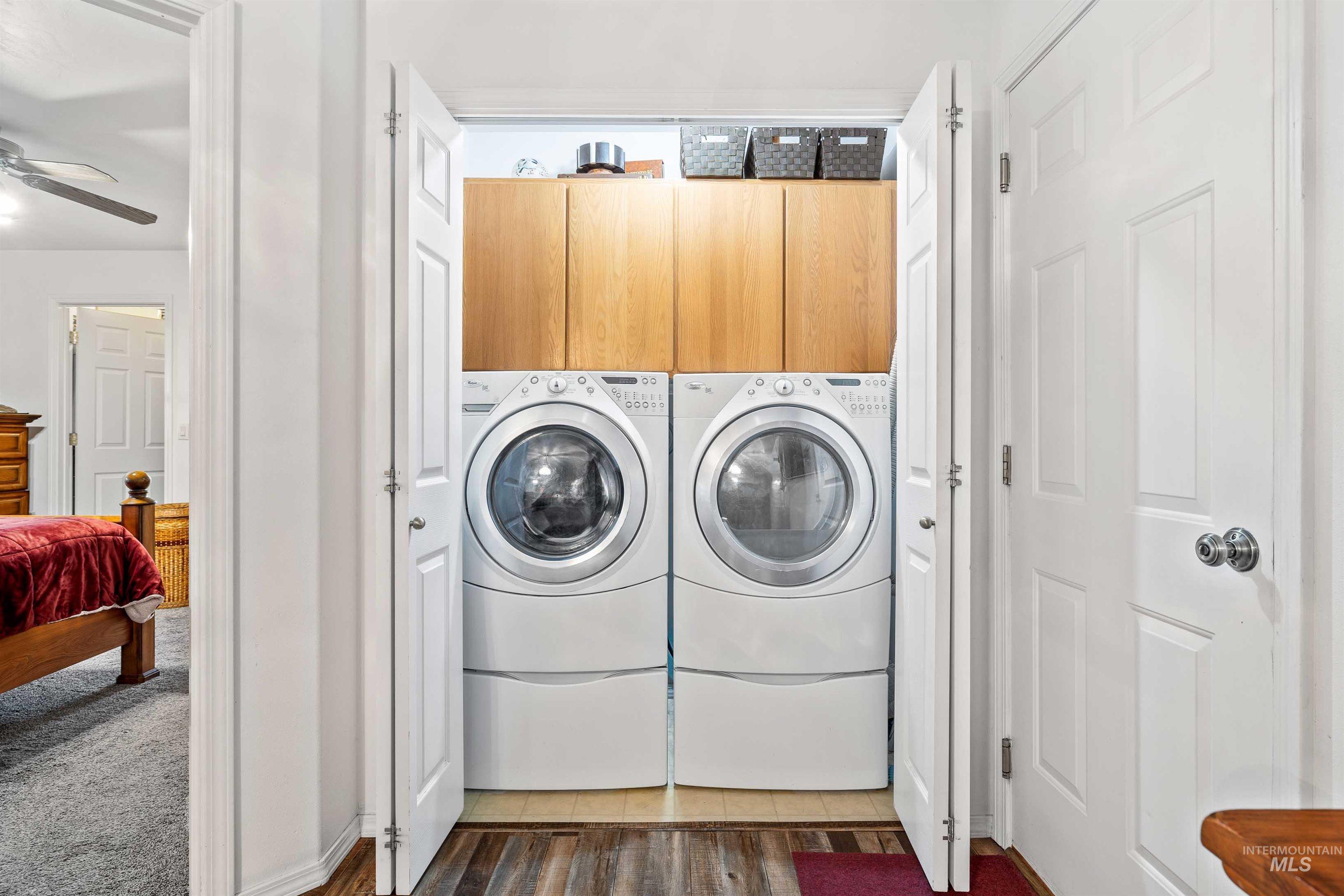 Washroom featuring dark wood finished floors, cabinet space, washer and clothes dryer, and a ceiling fan