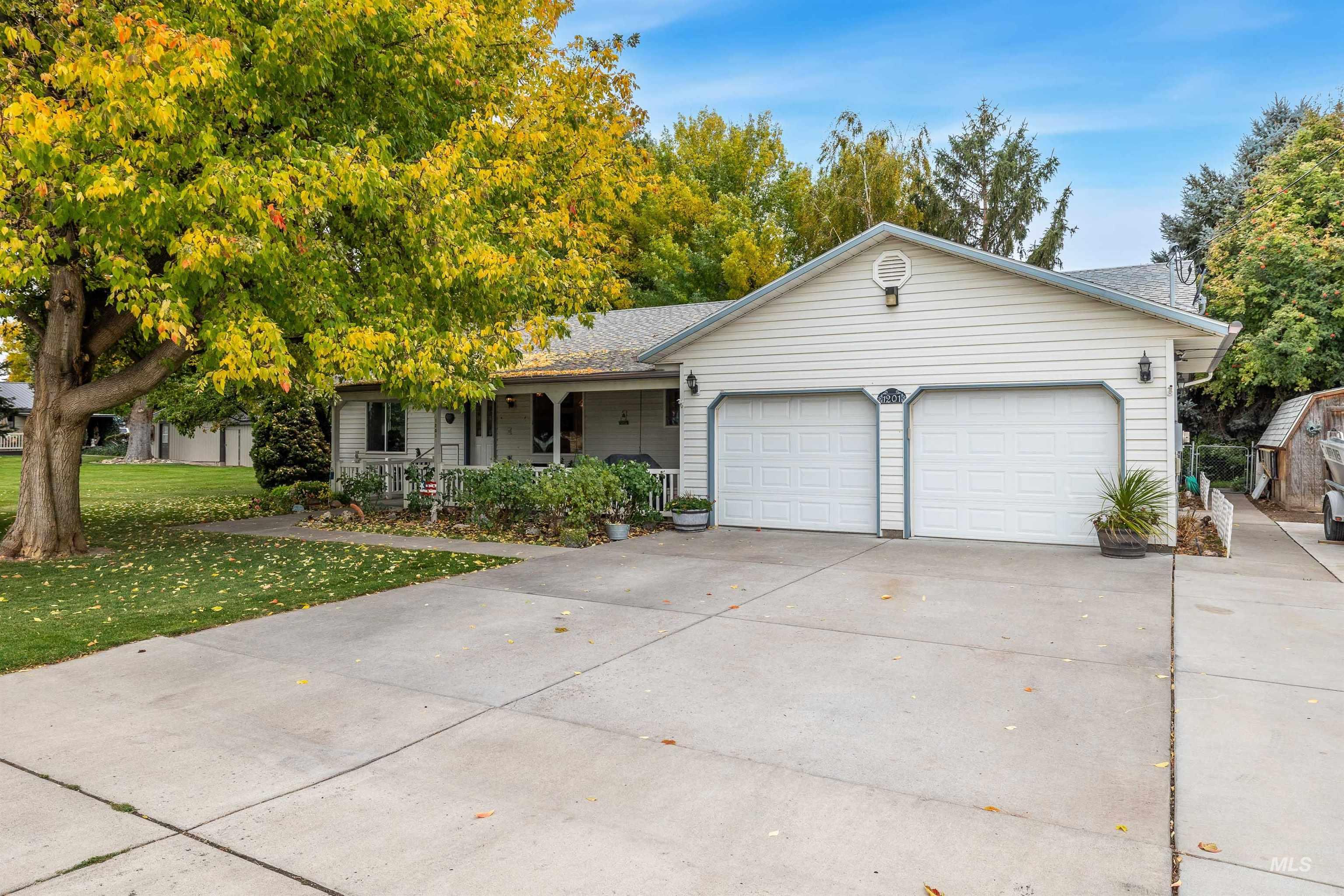 Ranch-style house with driveway, an attached garage, a shingled roof, covered porch, and a front lawn
