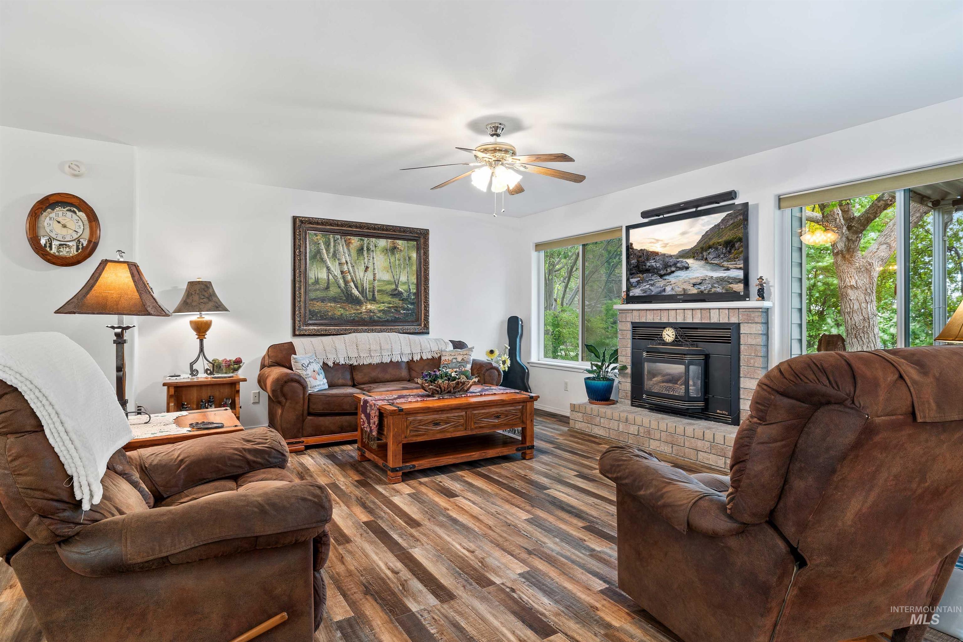 Living area featuring wood finished floors, a brick fireplace, and ceiling fan