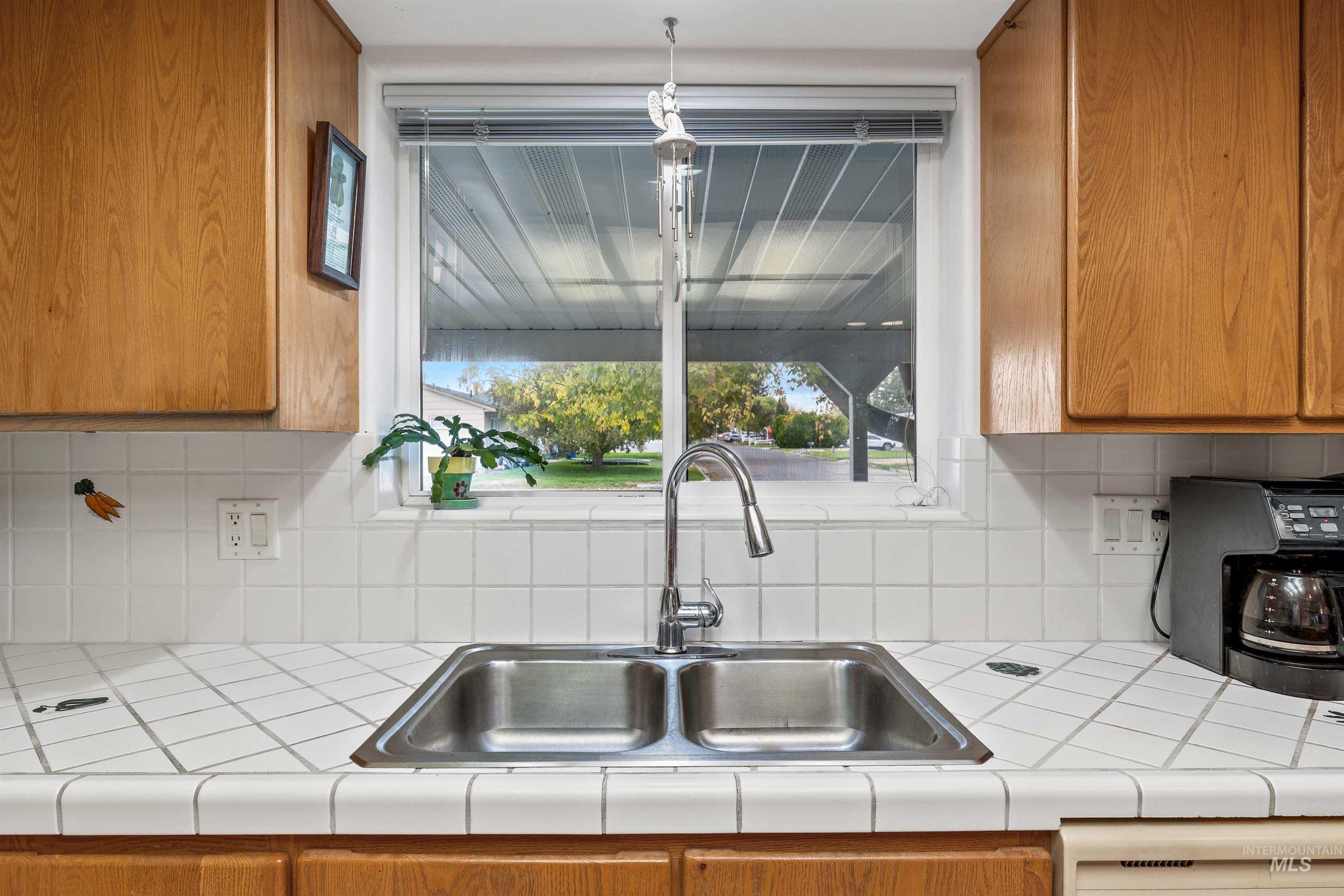 Kitchen featuring brown cabinets, decorative backsplash, tile countertops, and dishwasher