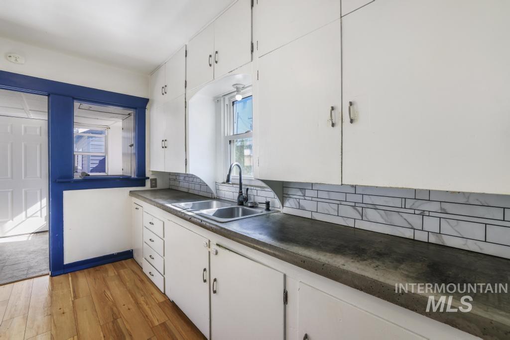 Kitchen featuring white cabinets, light wood-style flooring, backsplash, and dark countertops