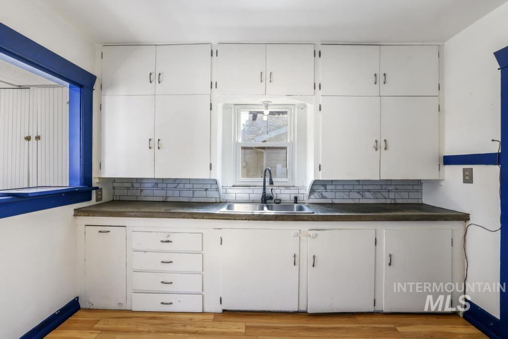 Kitchen with white cabinets, backsplash, light wood-type flooring, and dark countertops