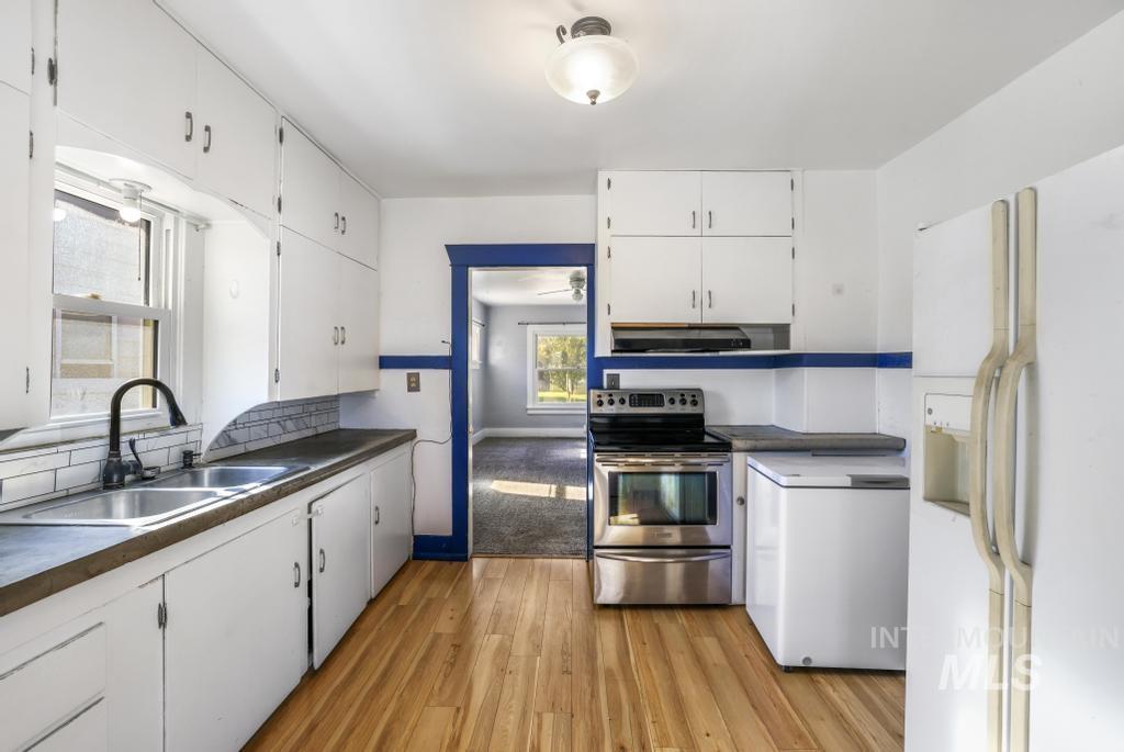Kitchen featuring white refrigerator with ice dispenser, stainless steel electric stove, white cabinets, light wood-type flooring, and dark countertops