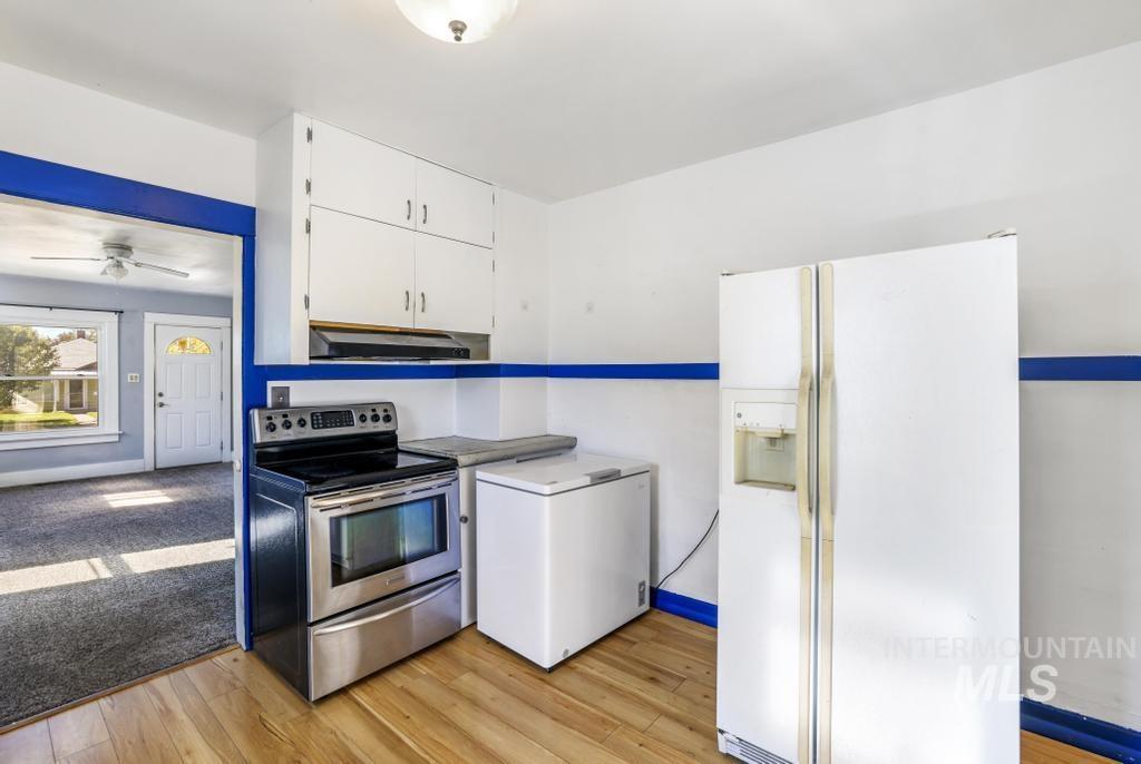 Kitchen featuring white refrigerator with ice dispenser, stainless steel electric range oven, white cabinetry, white fridge, and light wood-style floors