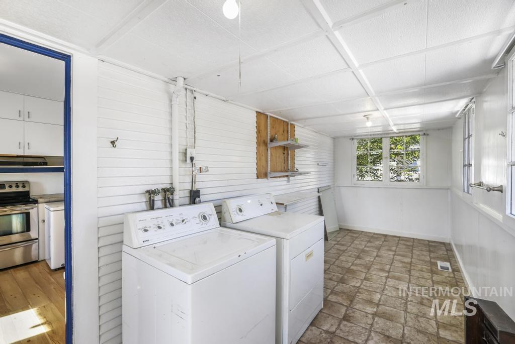Washroom featuring washing machine and clothes dryer, wood walls, and light stone finish flooring