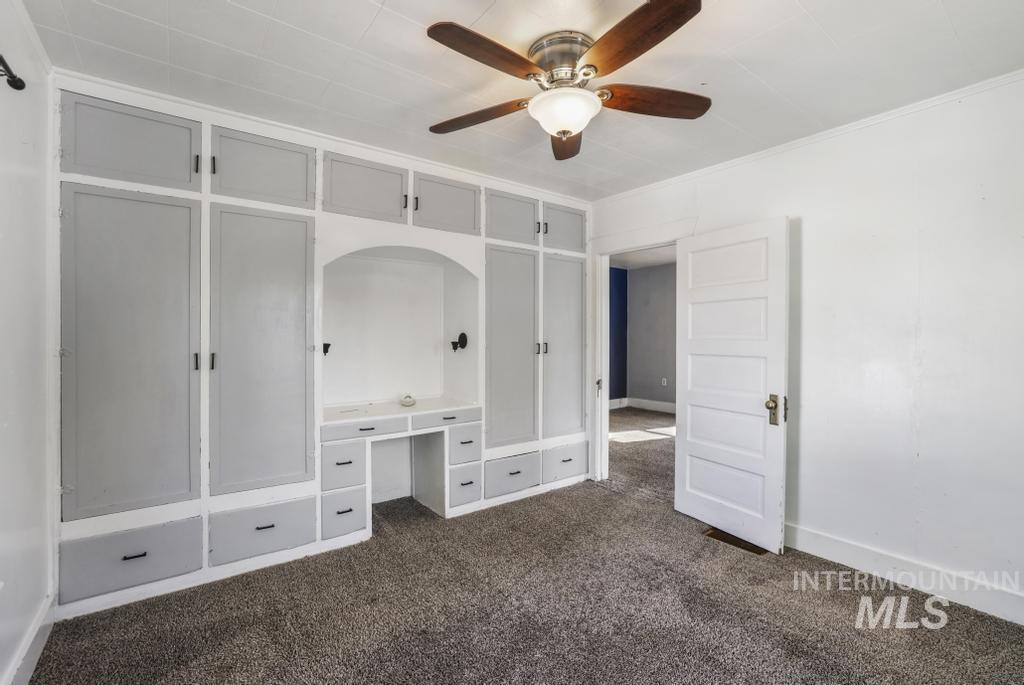 Unfurnished bedroom featuring dark colored carpet, a ceiling fan, an office area, and ornamental molding